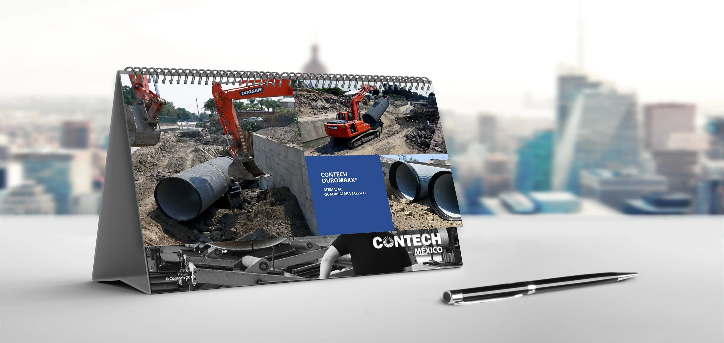 Calendar featuring construction site images with heavy machinery, pipes, and construction workers, marked with 'CONTECH DUROMAXX' and 'CONTECH MÉXICO', on a desk with a pen.