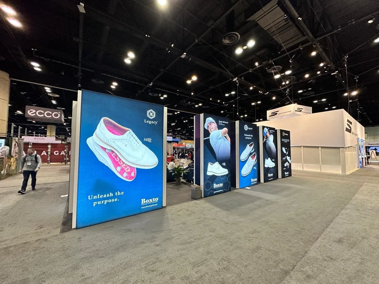 Exhibition booth displaying advertisements for Legacy and Boxto athletic shoes at a trade show.