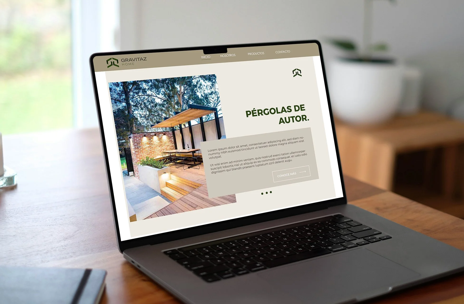 Laptop on a wooden table displaying a webpage for Gravitaz Home featuring an outdoor pergola with seating and plants.