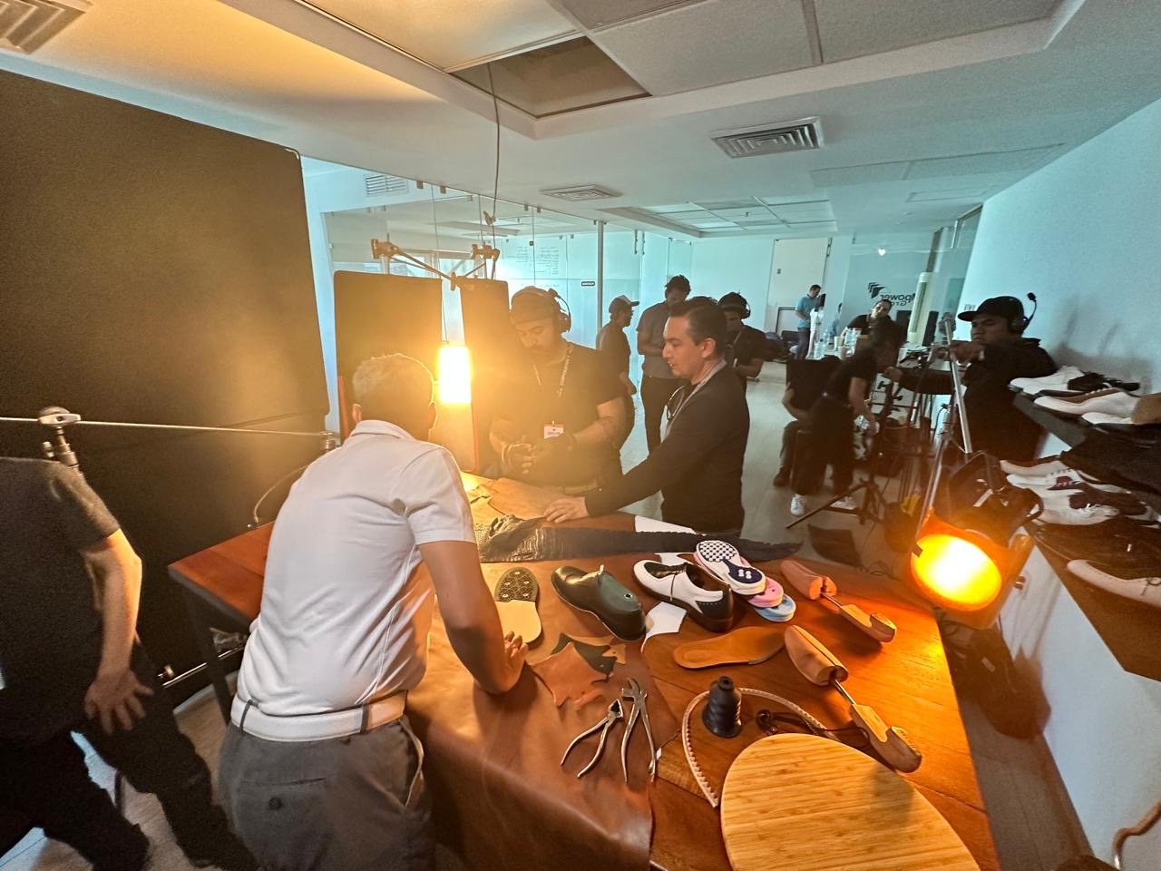 People working on shoe customization at a table in a busy workshop, with shoe-making tools and sneakers on the table.