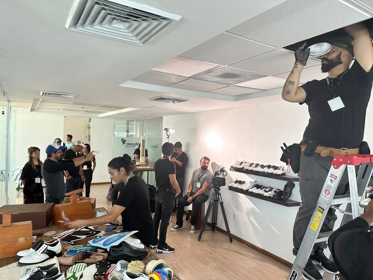 People setting up for a photoshoot or event in a retail space, with several individuals working on displays and a lounge area with shoes on shelves.