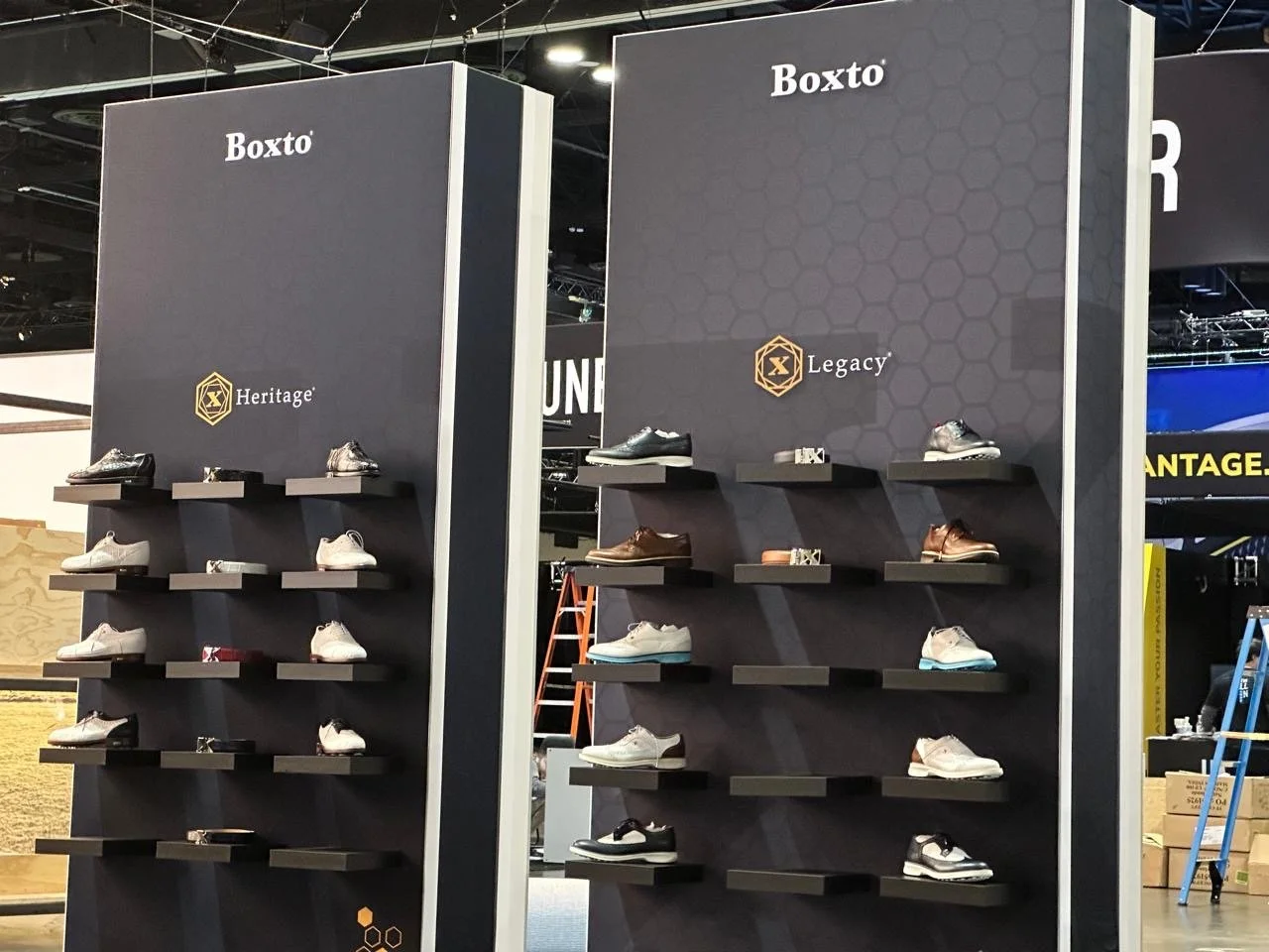 Display of various shoes on shelves at a retail store, with branding for 'Boxto,' 'Heritage,' and 'Legacy'.