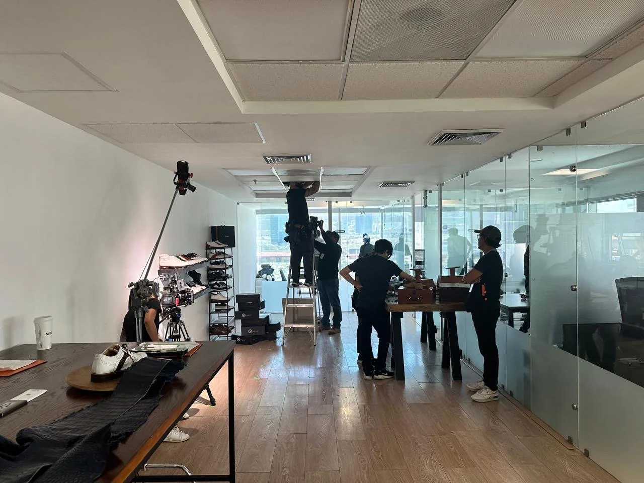 Recording studio with people preparing for filming, equipment, and a camera on a tripod pointing toward a person working on the ceiling.