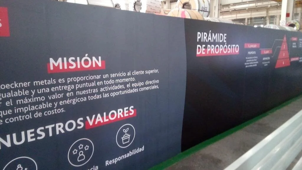 An informational display with sections titled "MISION," "NUESTROS VALORES," and "Pirámide de Propósito" in Spanish, featuring text and icons on a black background with some red highlights.