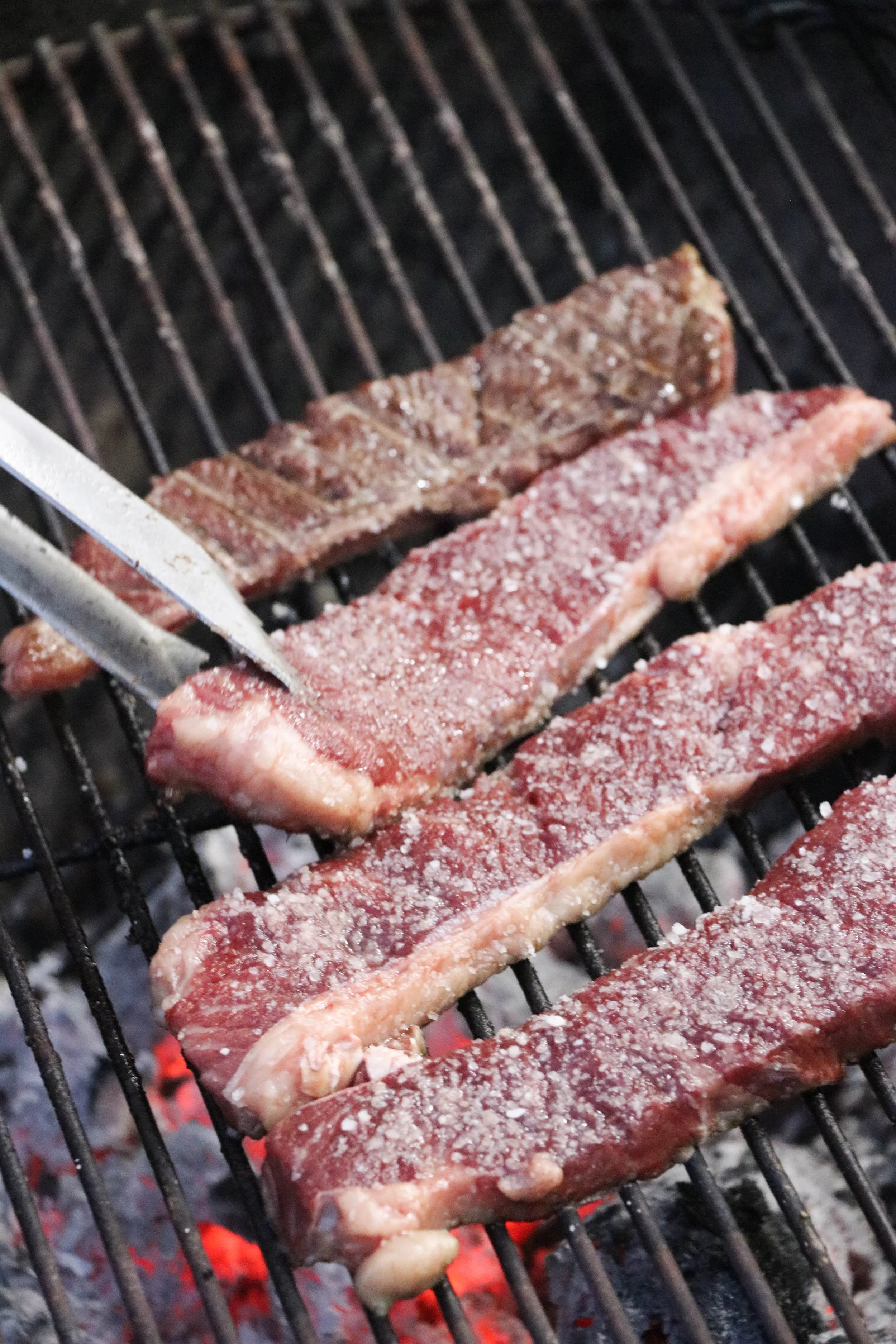 Beef steaks grilling on a barbecue grill with salt seasoning on top.
