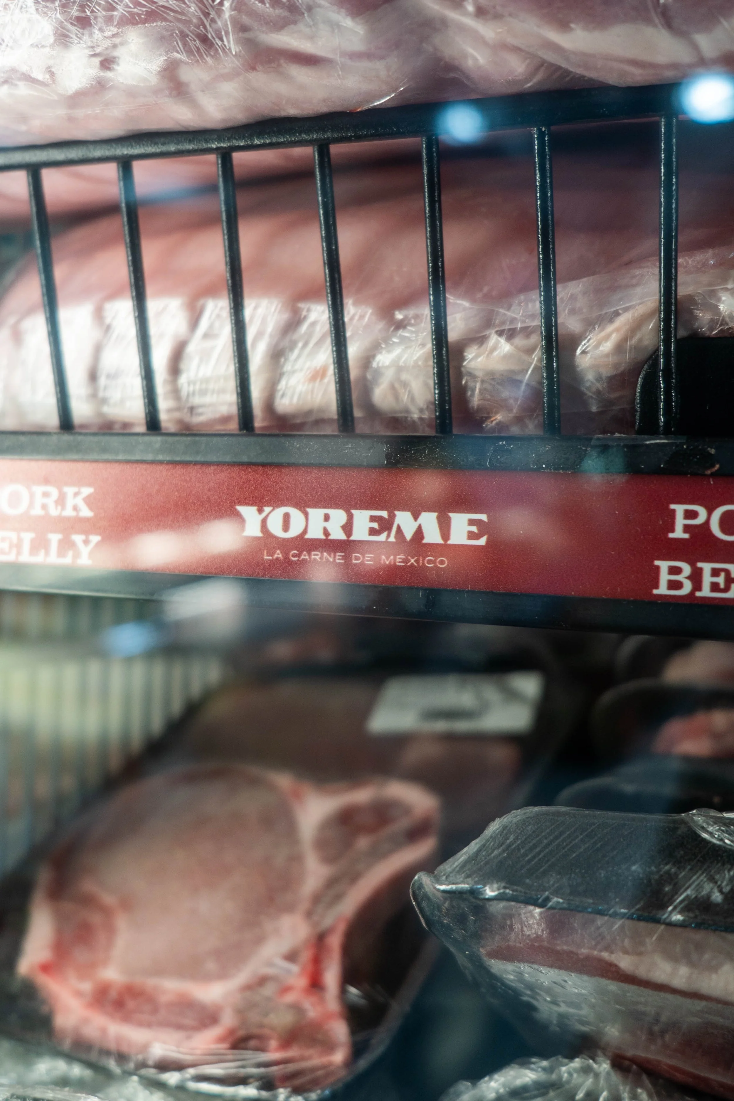 Frozen cuts of meat in a grocery store freezer, with visible packaging and a sign reading 'YOREME La Carne de México'.