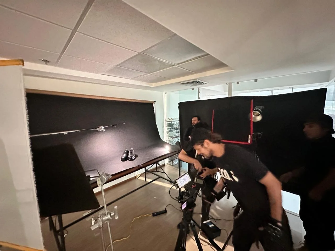 Photo of a photography studio with black backdrops and professional equipment, with three men preparing for a photo shoot.