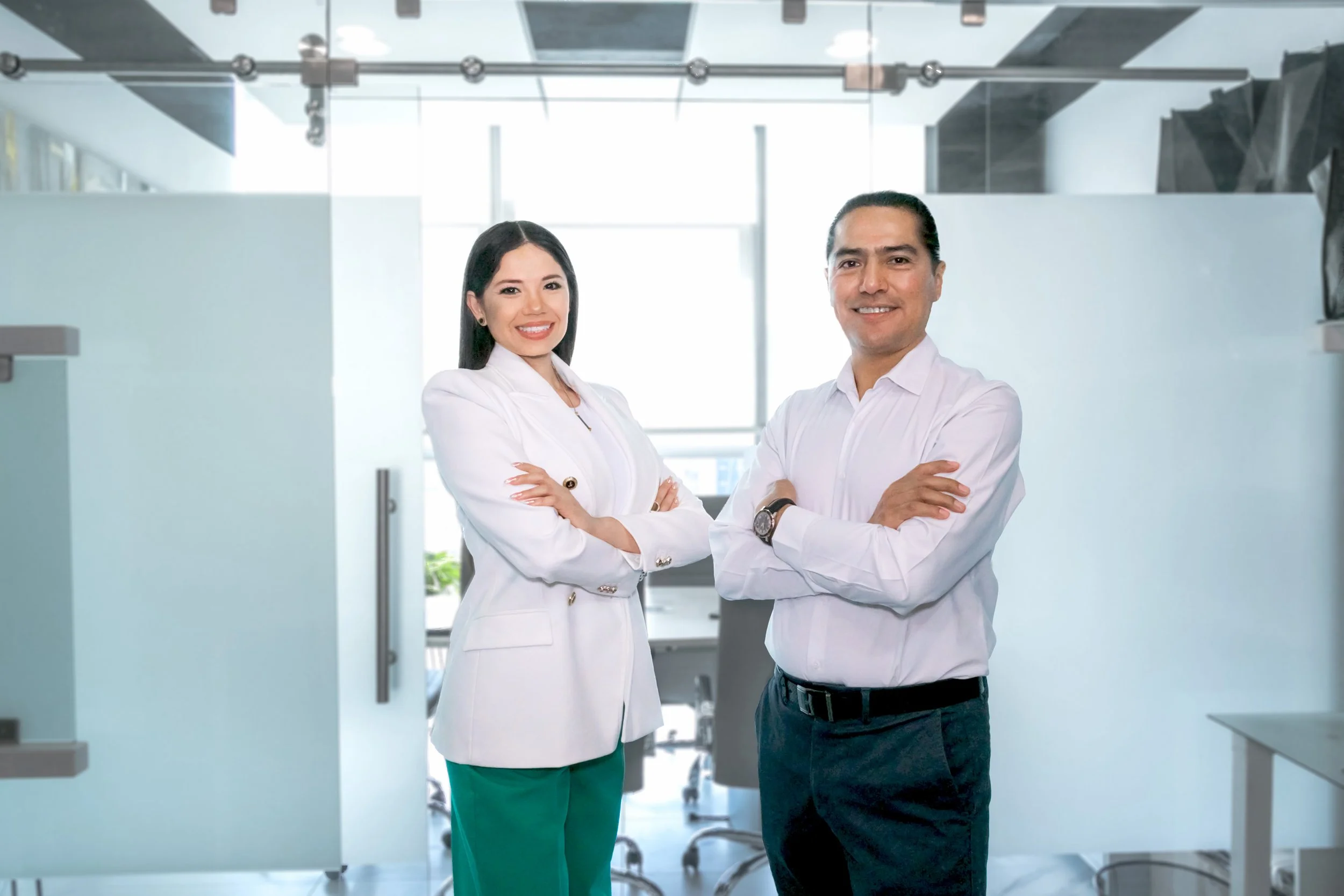 Two healthcare professionals, a woman and a man, standing in a modern medical office or clinic with arms crossed, smiling at the camera.