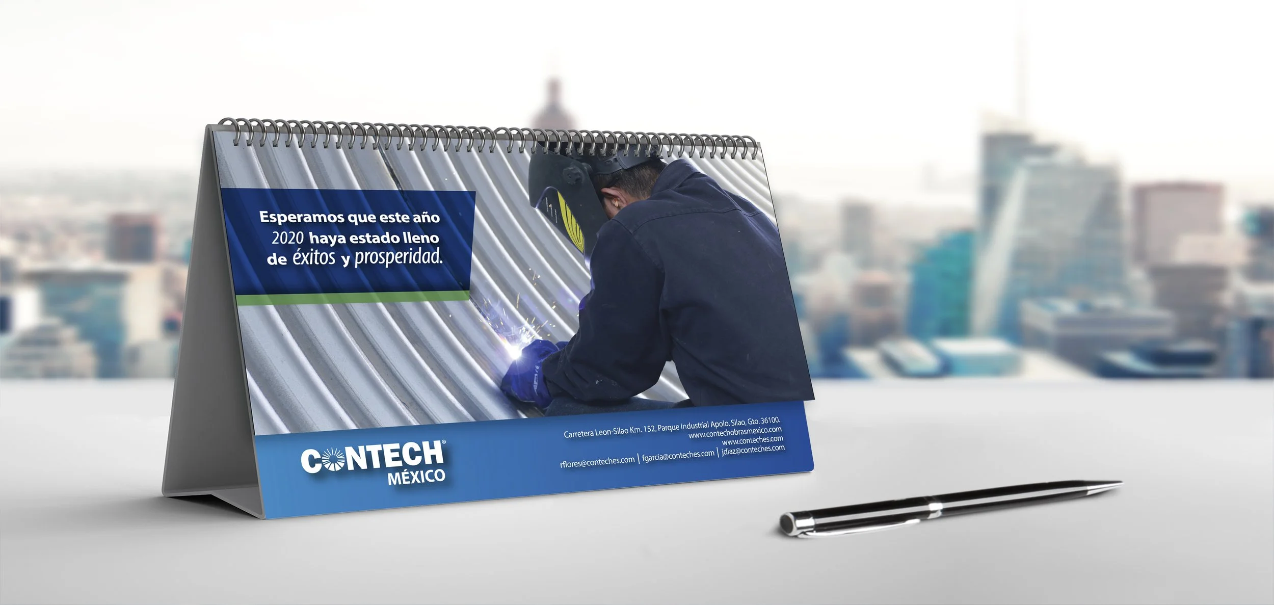 Desk calendar with a photo of a worker welding steel, overlaid with a message wishing success and prosperity in 2020, with contact information for CONTECH Mexico and a pen nearby.