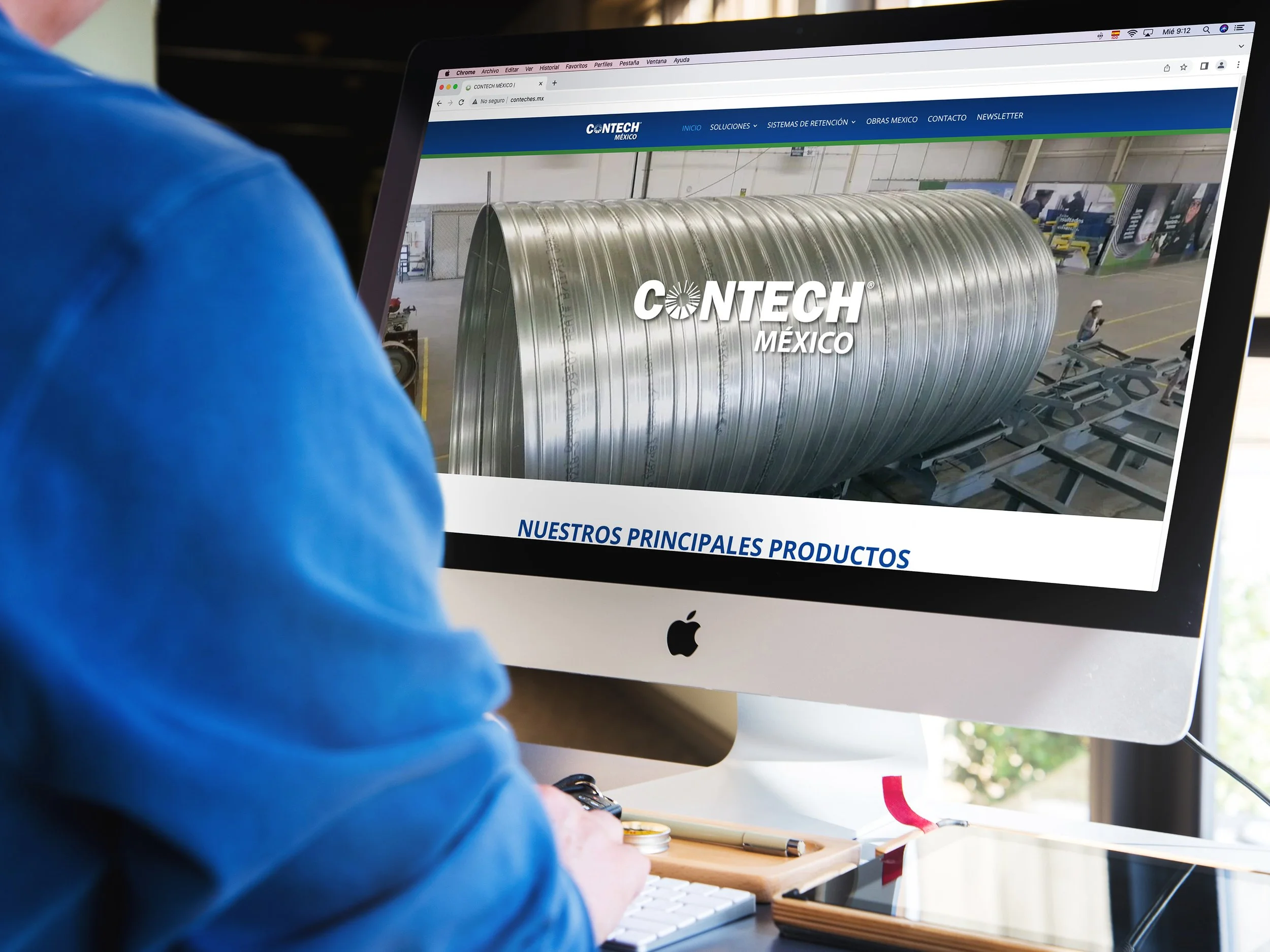 Person browsing the Contech México website on an iMac computer, showing a large metallic structure inside a factory.