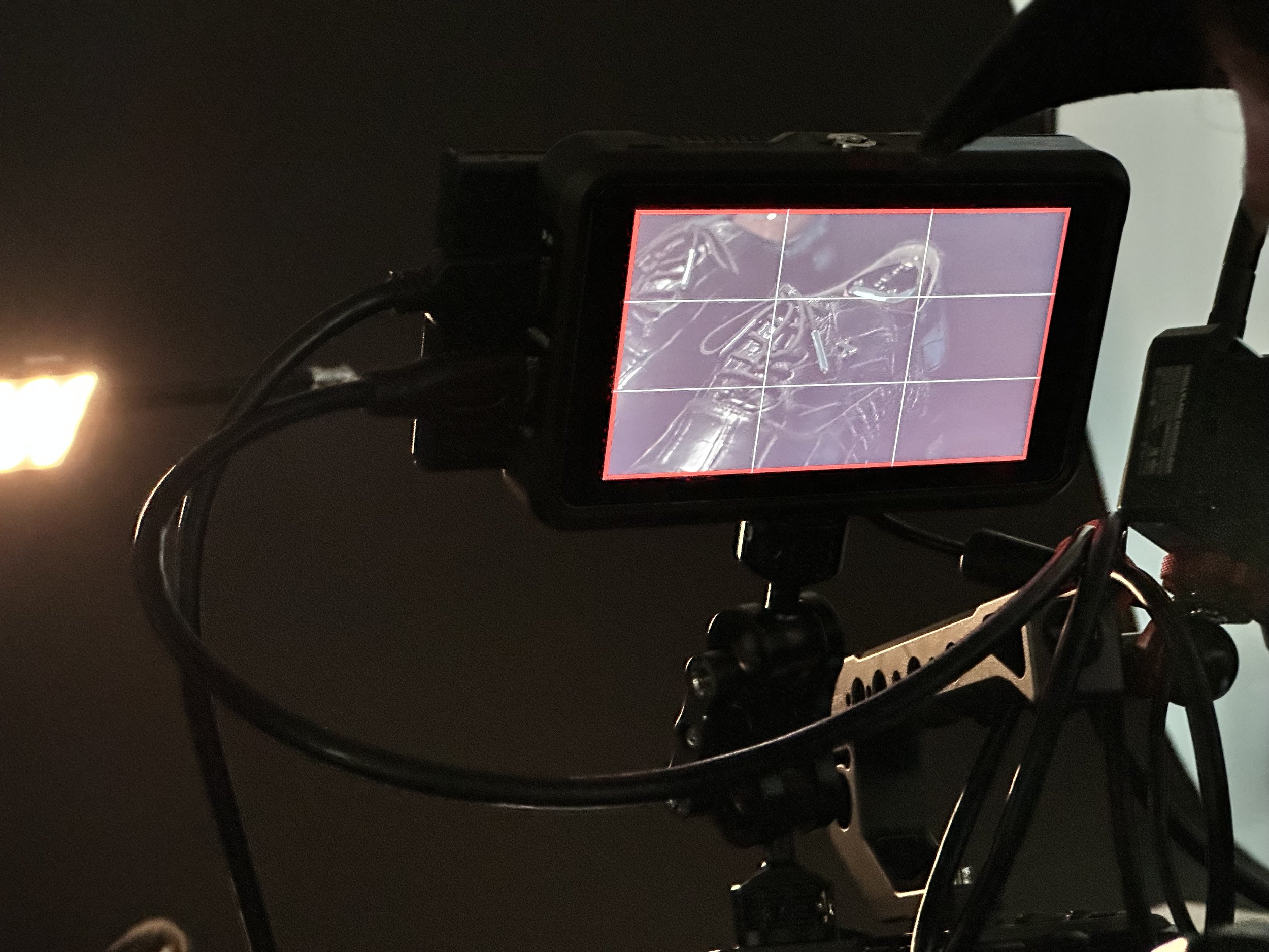 A camera monitor shows a robotic arm with detailed joints and parts, positioned in a dark environment with a light source on the left.