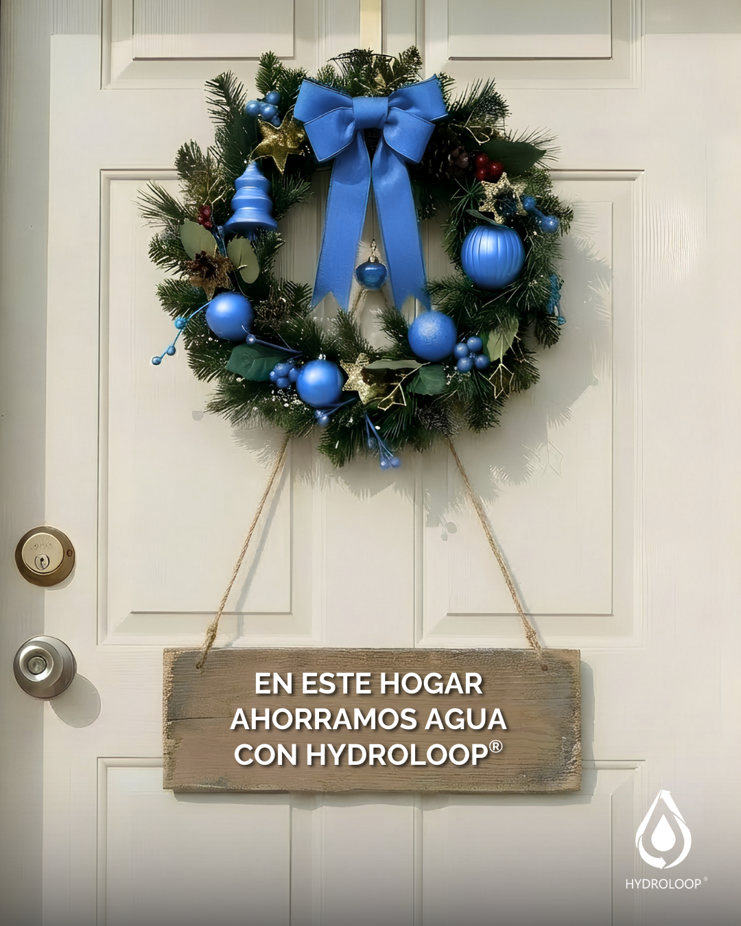 Christmas wreath with blue ornaments, gold stars, and a large blue bow, hanging on a white door, with a wooden sign beneath it that says, 'En este hogar ahorramos agua con Hydroloop'.