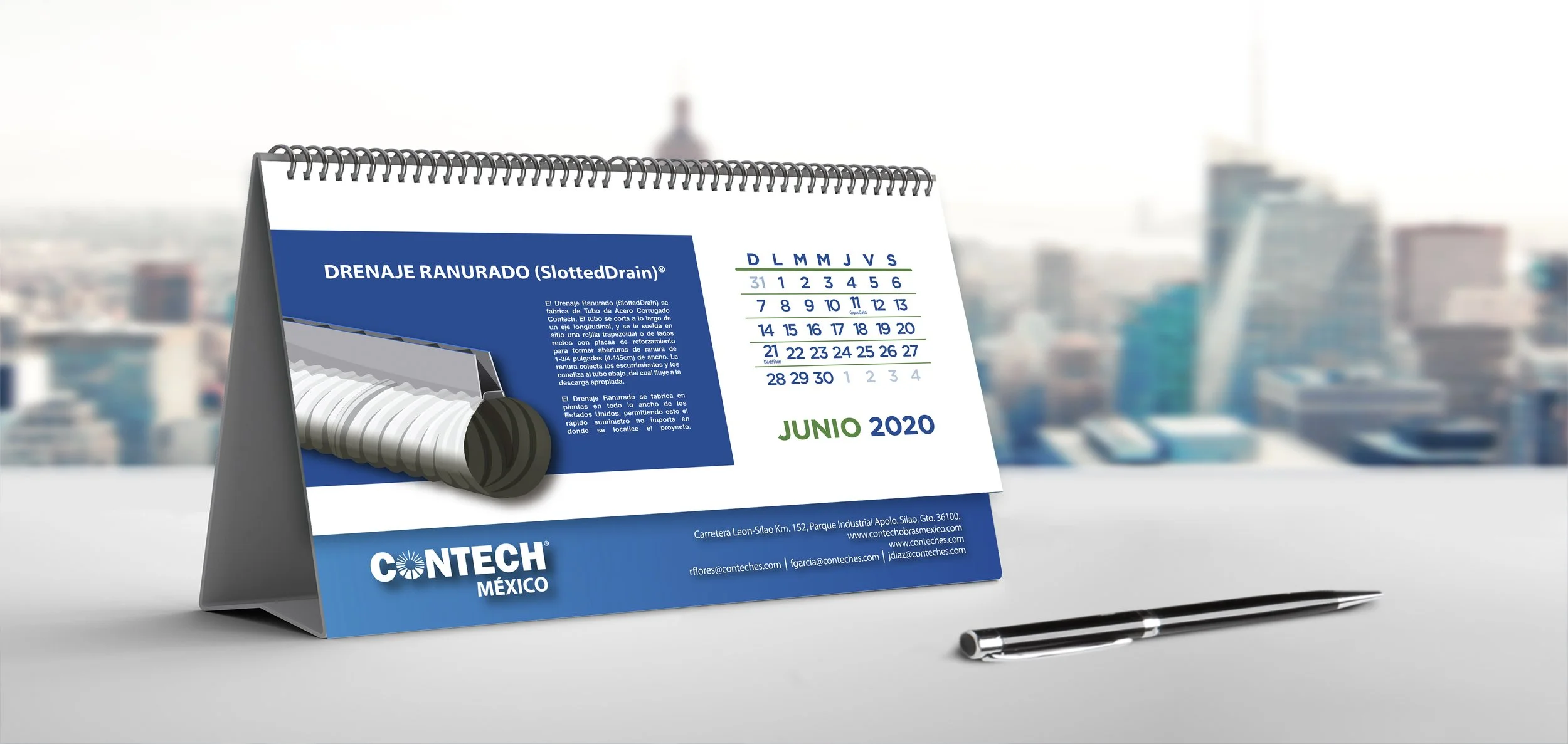 Desk calendar displaying June 2020 with a blue and white design and a pen placed on a white surface, with a blurred cityscape in the background.