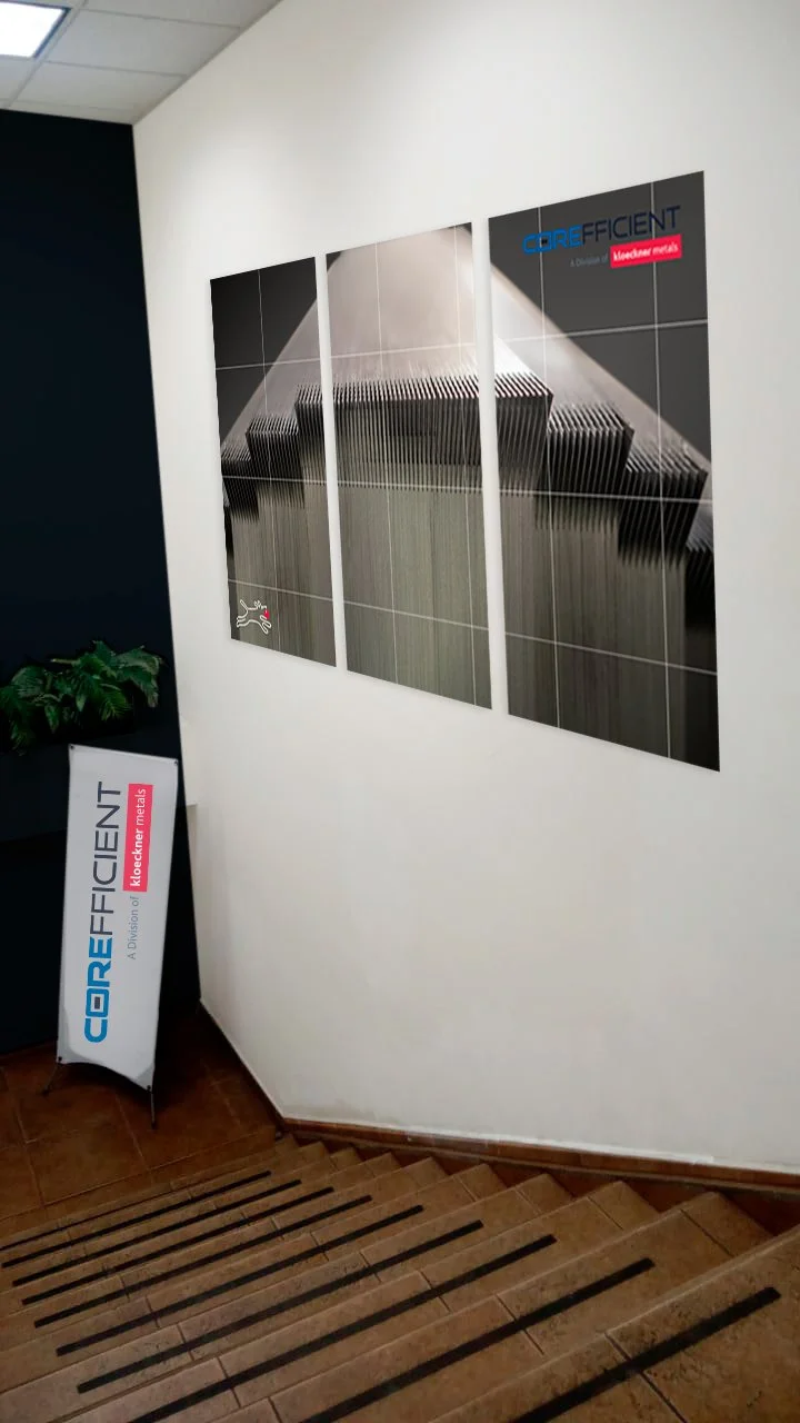 Photograph of a modern office stairwell with a three-panel abstract artwork on the wall, a sign displaying the company name COREfficient, and a potted plant on the landing.