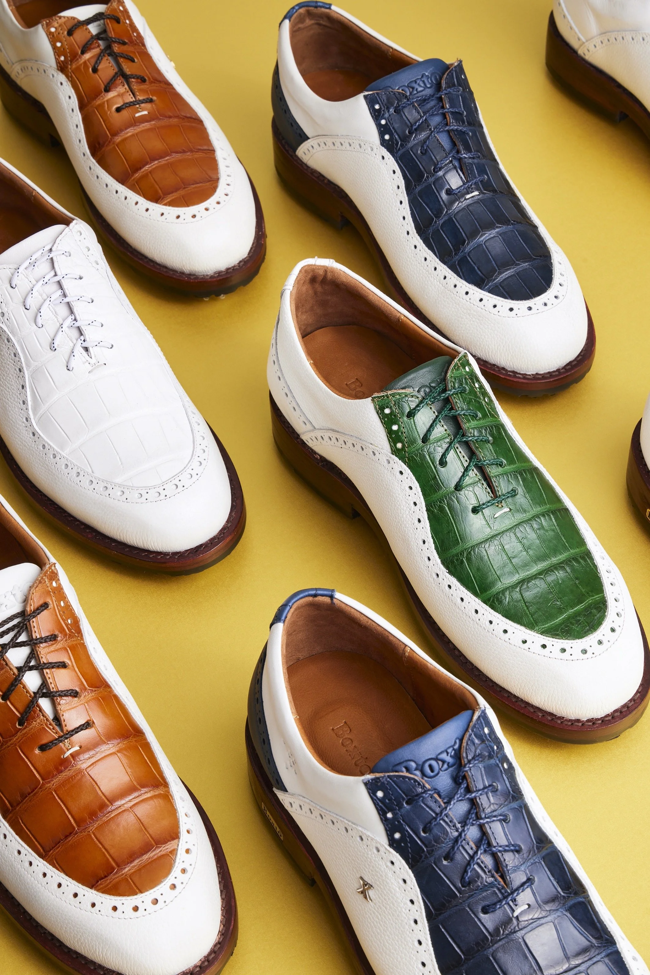 Colorful men's dress shoes with crocodile and alligator patterns, in shades of brown, navy, green, and white, arranged on a yellow background.