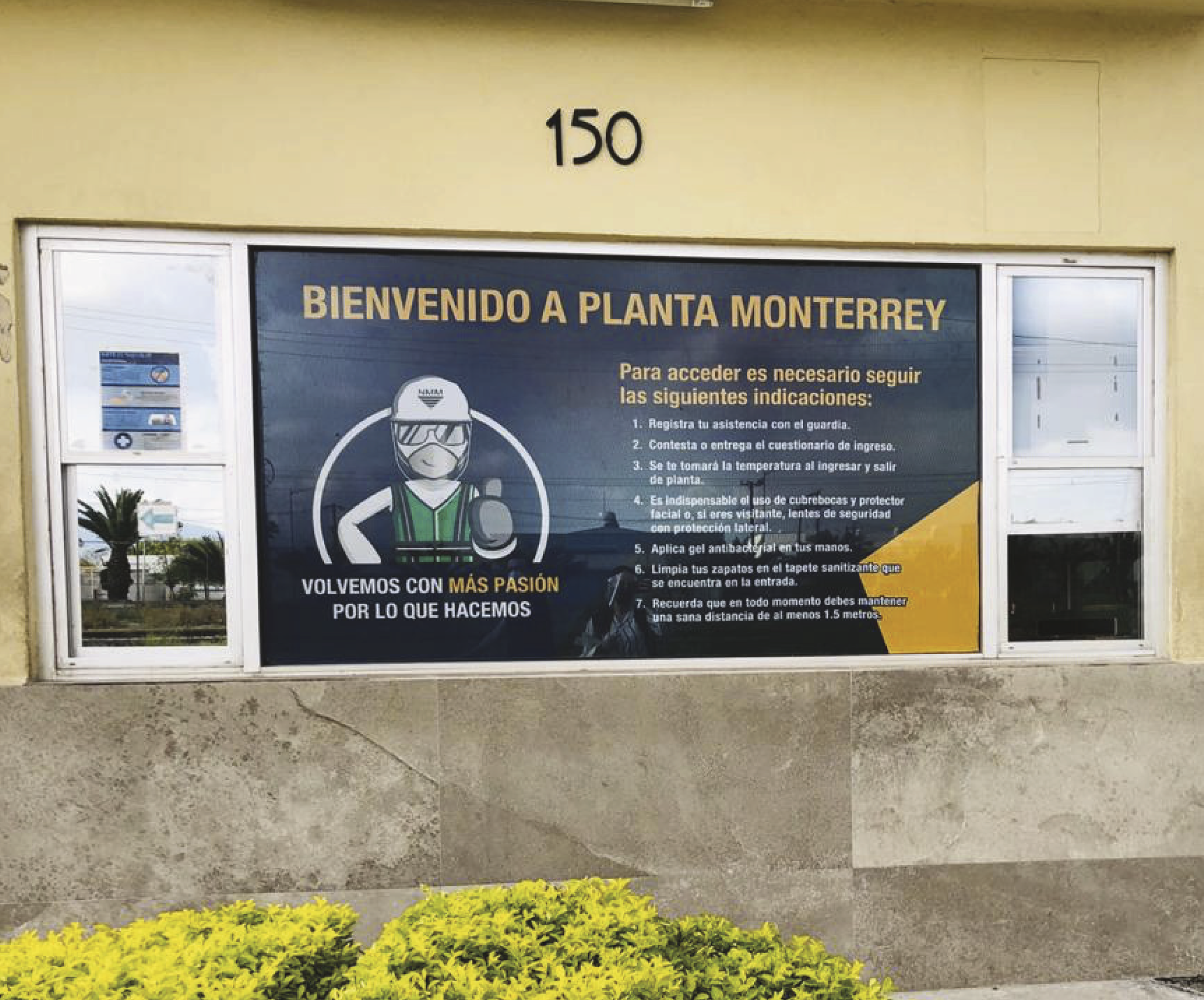 Sign welcoming visitors to Planta Monterrey with safety instructions in Spanish, including wearing masks, disinfecting shoes, maintaining distance, and using hand sanitizer.