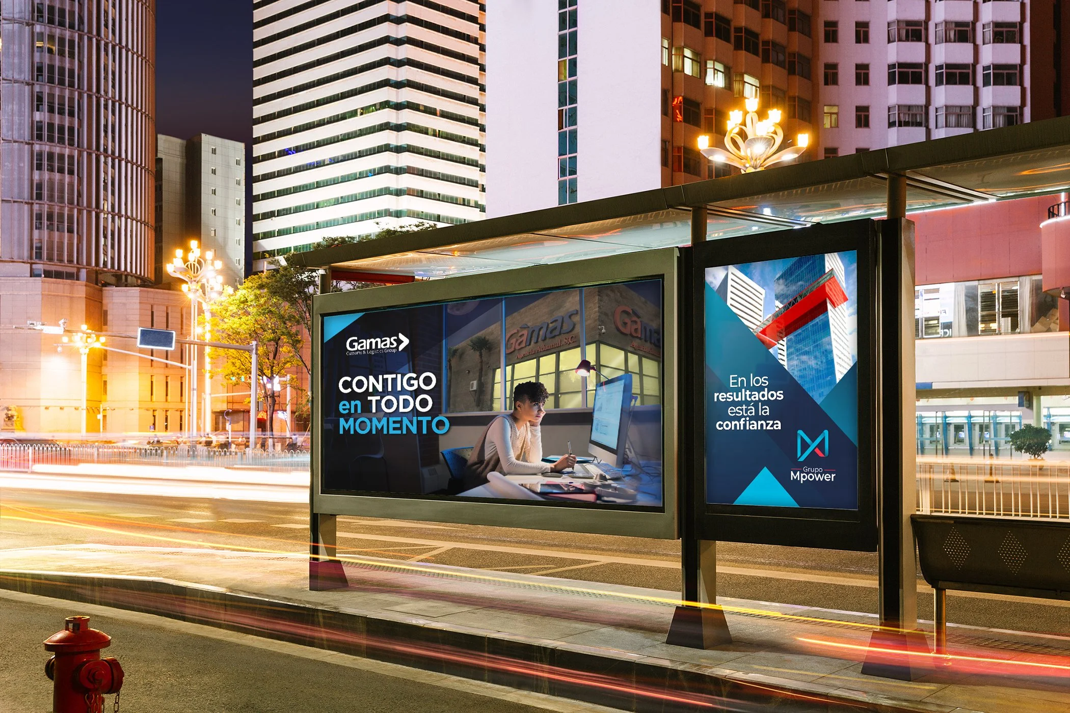 Bus shelter with illuminated advertisements in an urban city at night, tall buildings, light trails from moving vehicles.