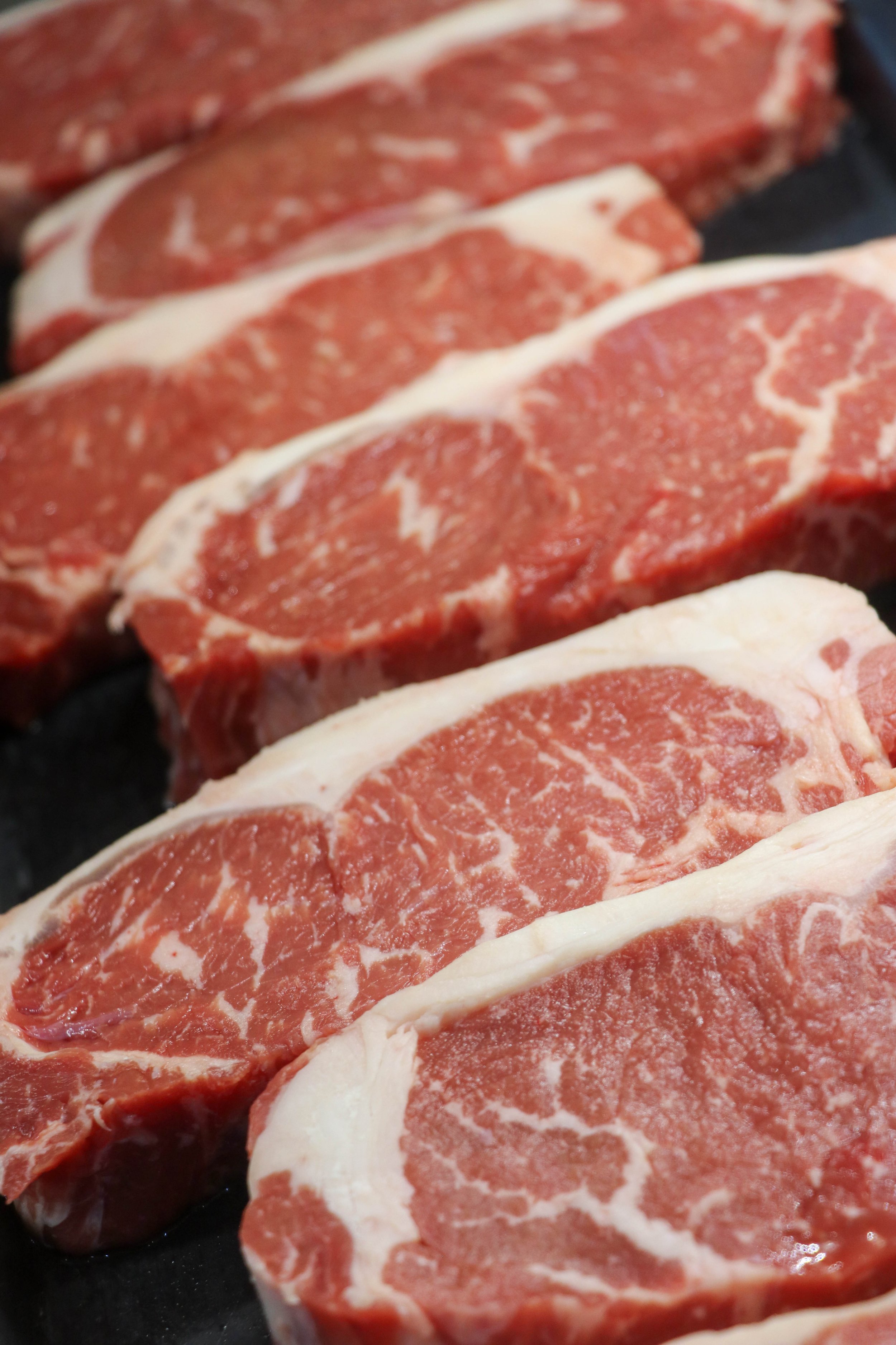 Several raw beef steaks with marbling on a black surface.