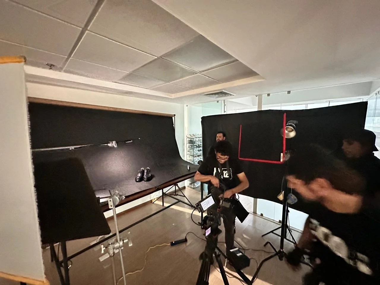 Studio setup with black backdrop, photography equipment, and three people preparing for a photoshoot or filming.