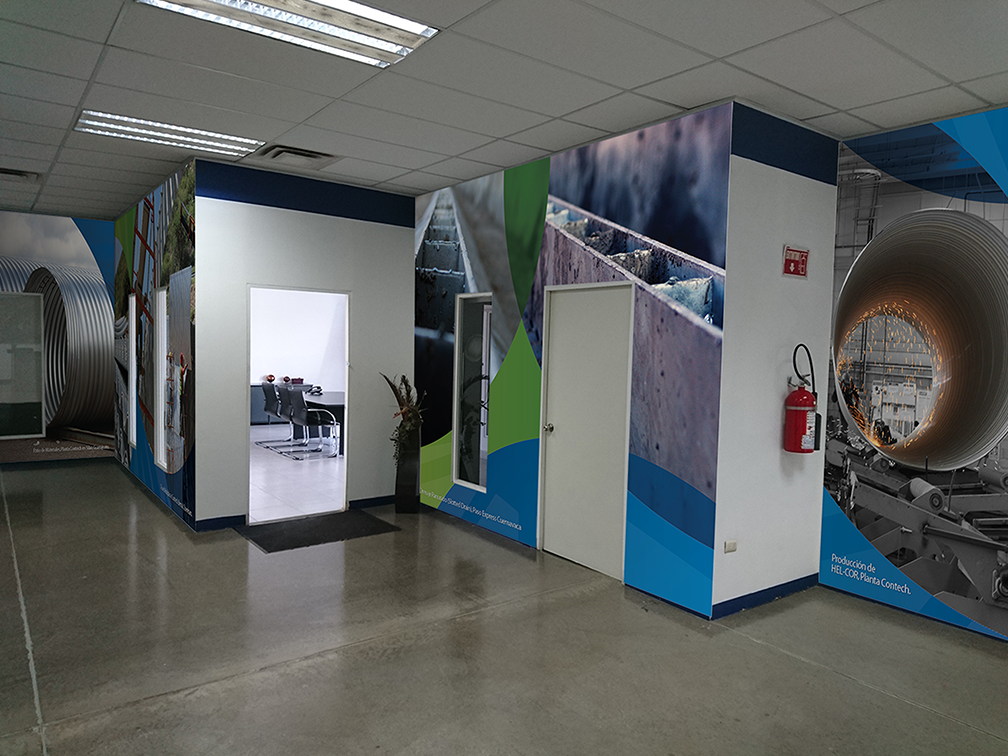 Indoor office corridor with wall murals of industrial machinery, a conference room visible through an open door, and a fire extinguisher mounted on the wall.