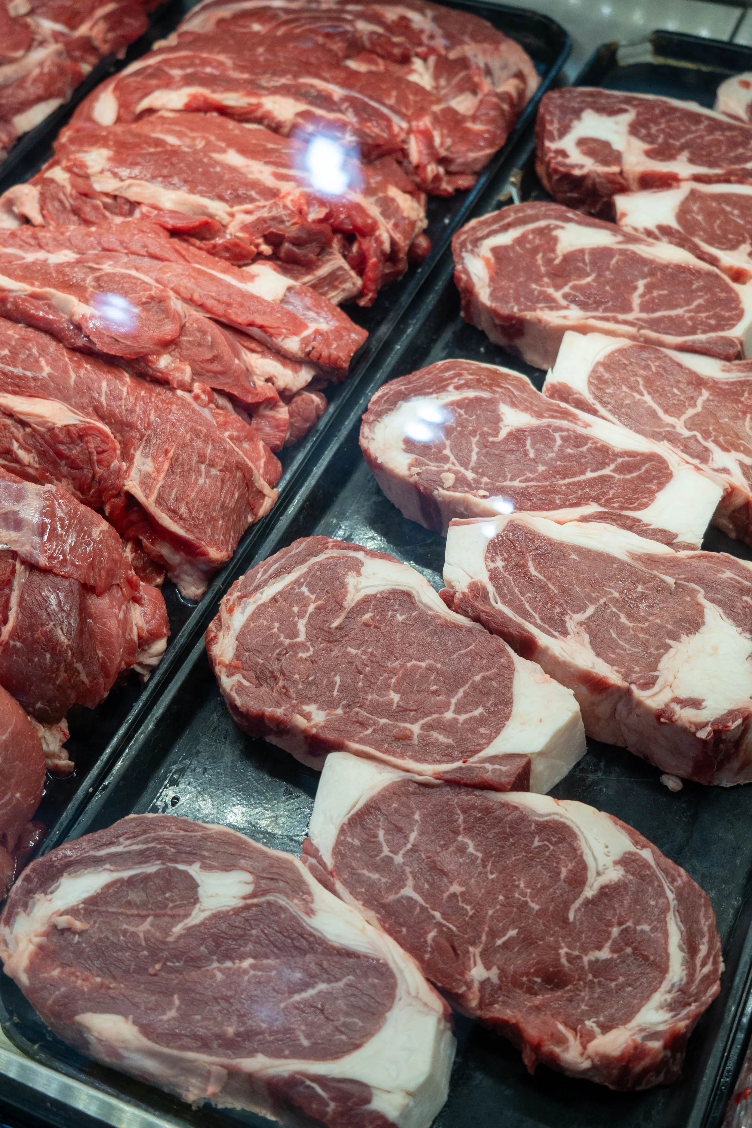 Display of raw beef steaks at a grocery store or butcher shop, featuring different cuts including ribeye and sirloin.