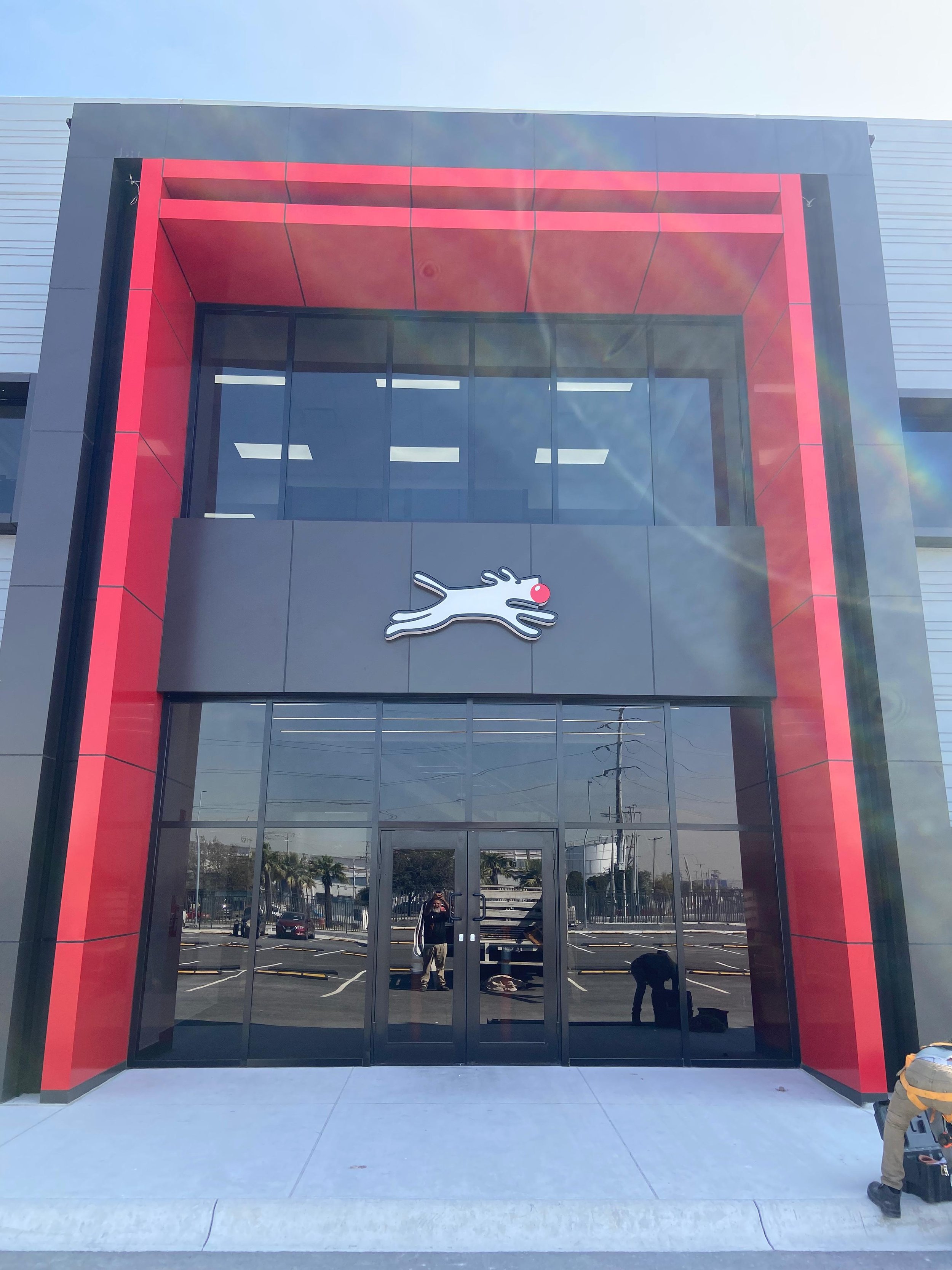 Exterior of a modern building with black and red accents, featuring a logo of a stylized rabbit with a red nose above the entrance.