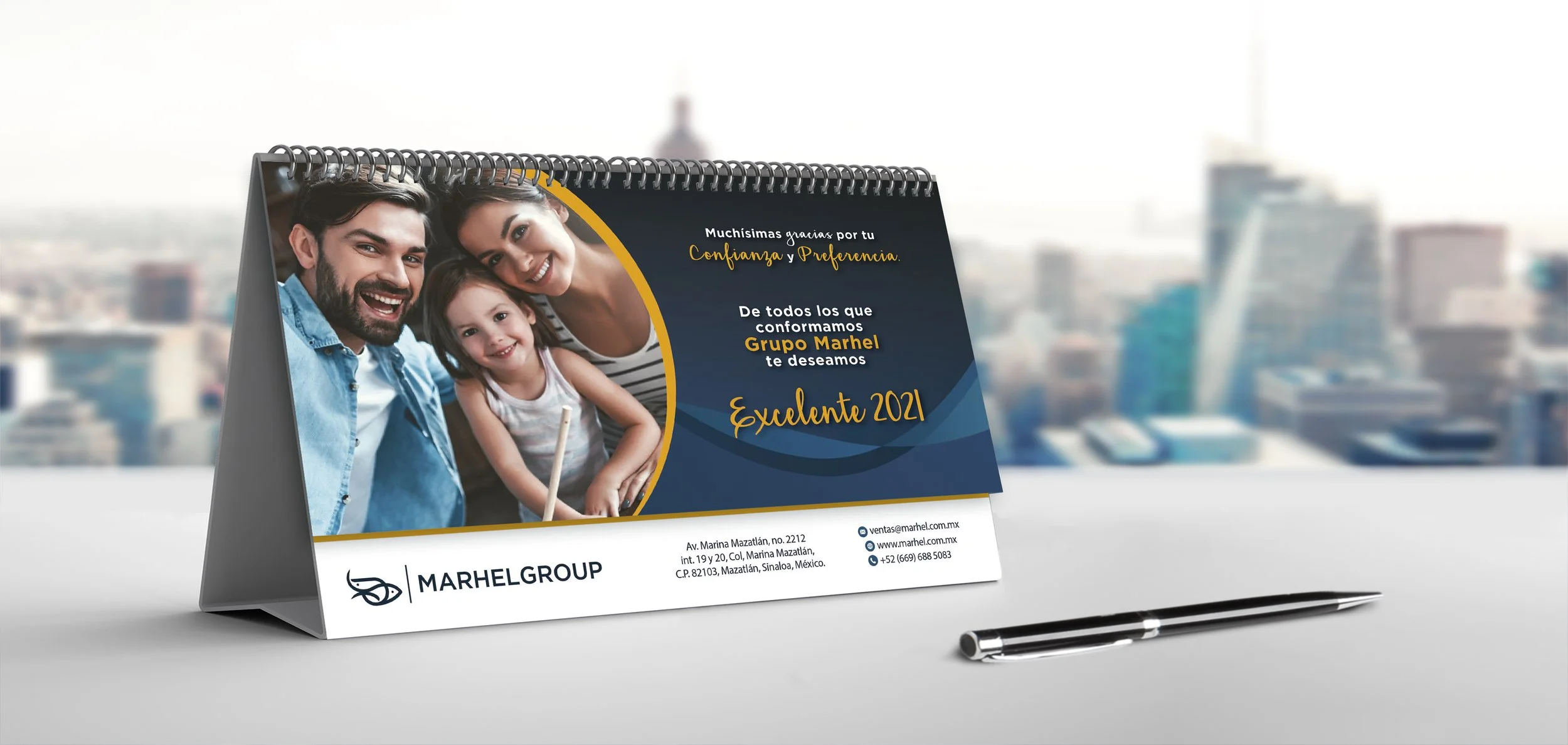A desk calendar on a white surface displaying a family photo of a smiling man, woman, and child, with contact information and a message of gratitude and good wishes for 2021 from Marhel Group.