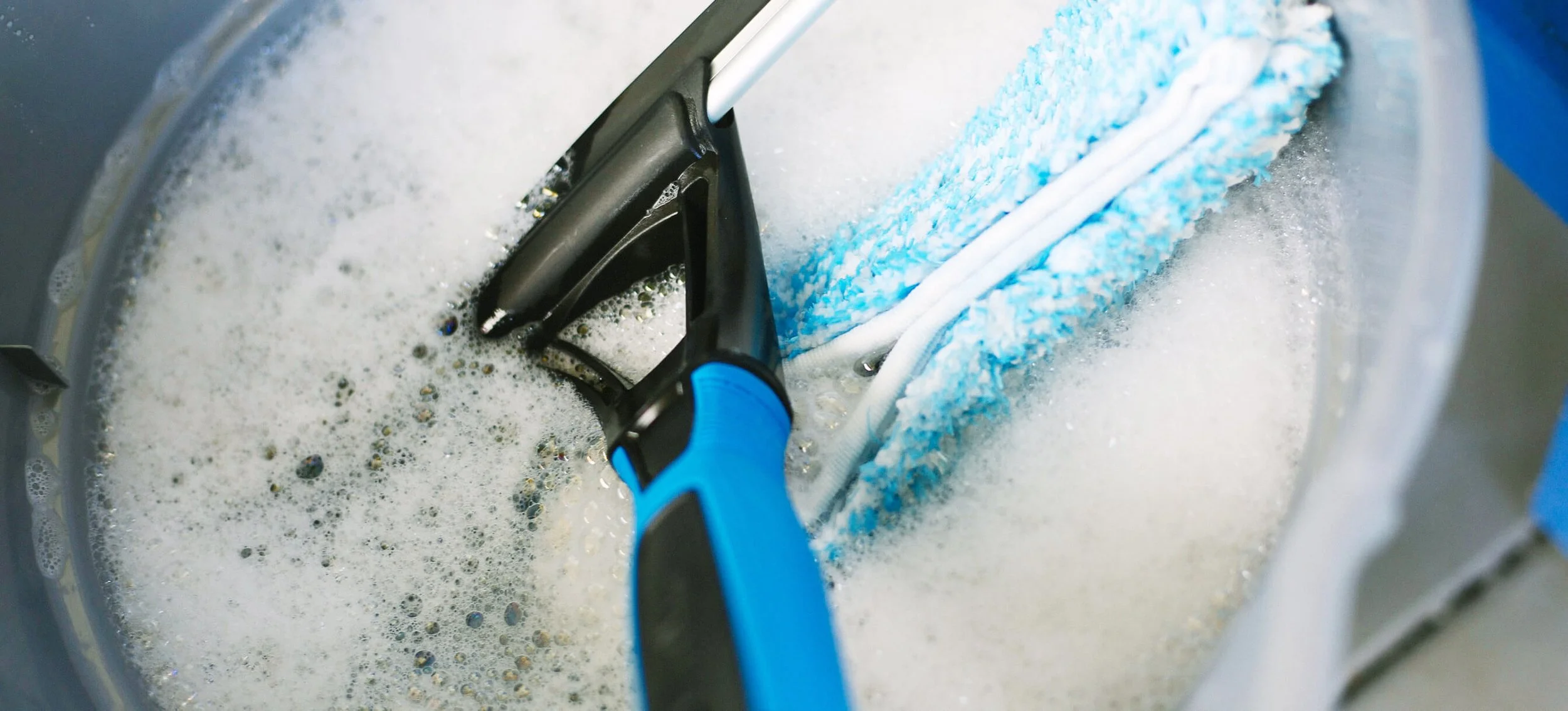 A blue and black scrub brush cleaning a washing machine drum with soap suds and foam.