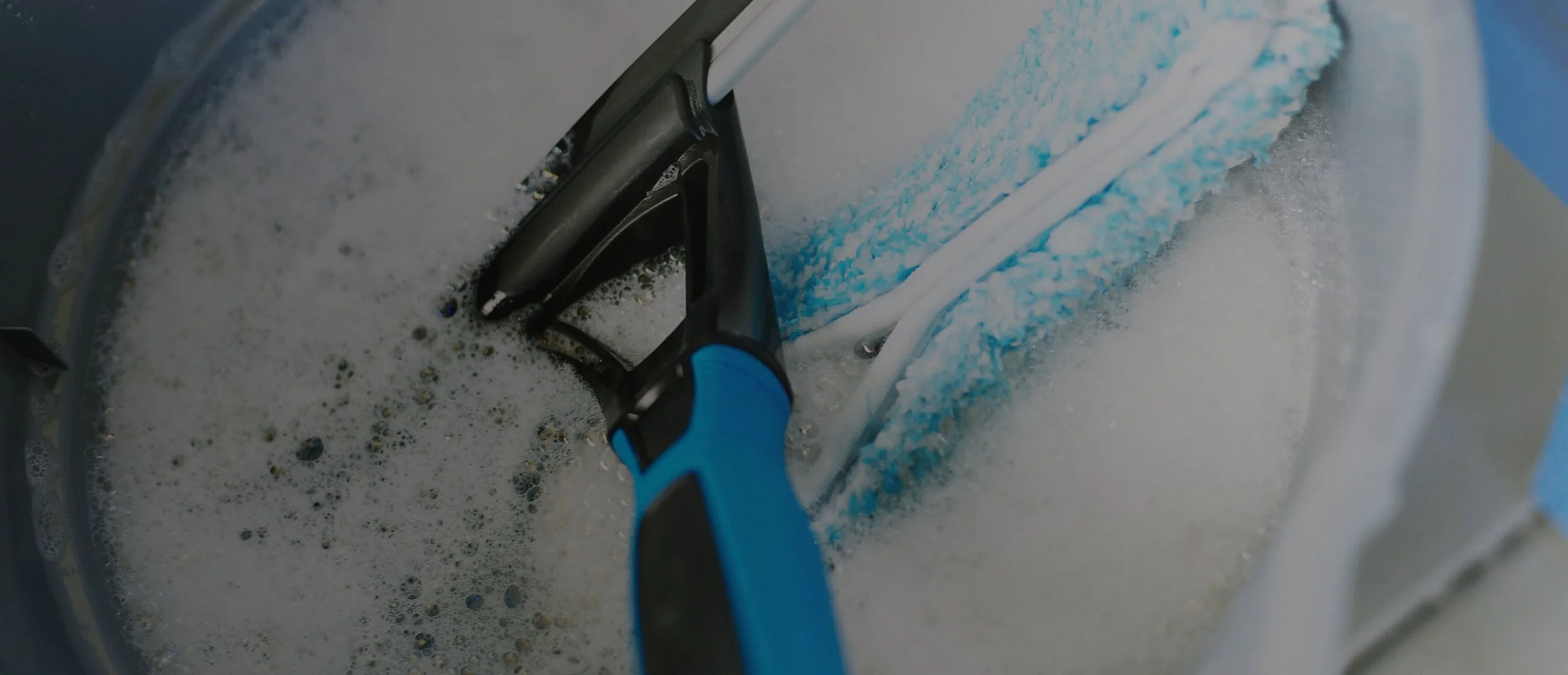 Close-up of a blue sponge with a washing brush inside a washing machine filled with soapy water.