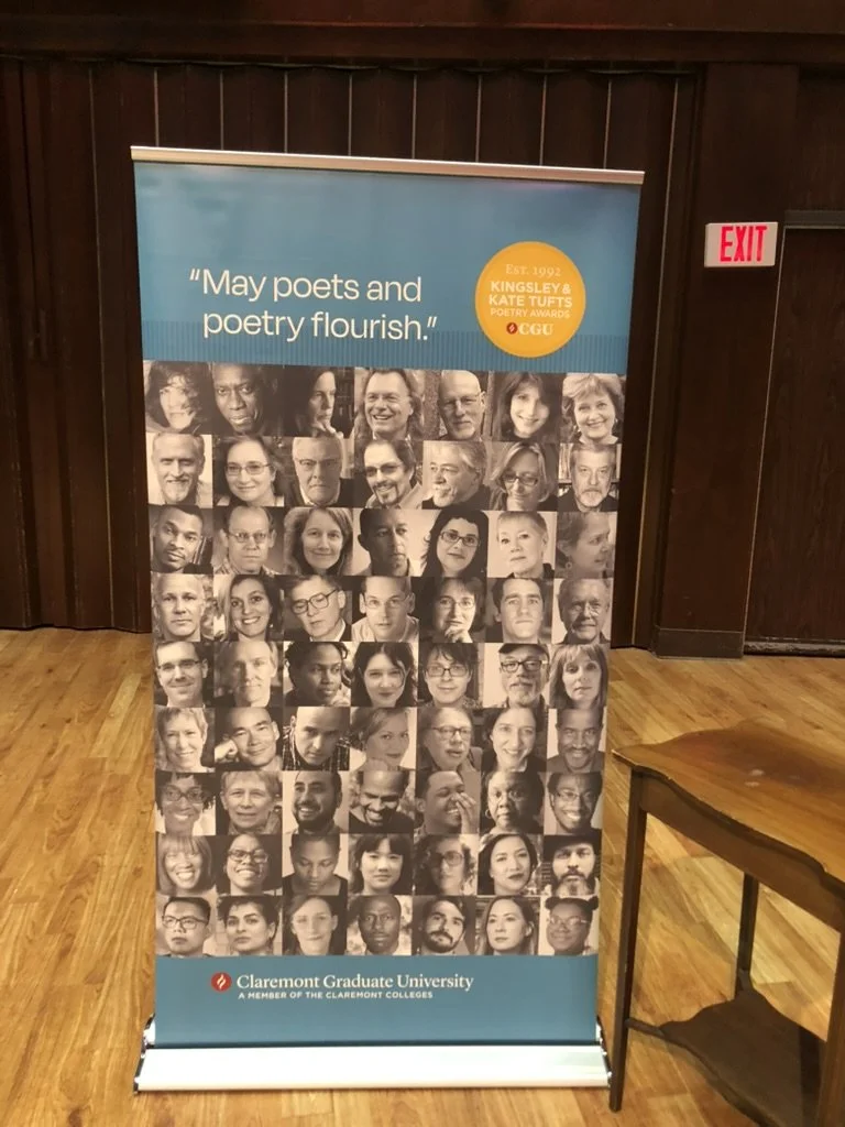 A photo of a pop-up banner featuring pictures of past winners of the Kingsley & Kate Tufts Poetry Award Winners from 1992 to the present. The award is presented by the Claremont Graduate University.