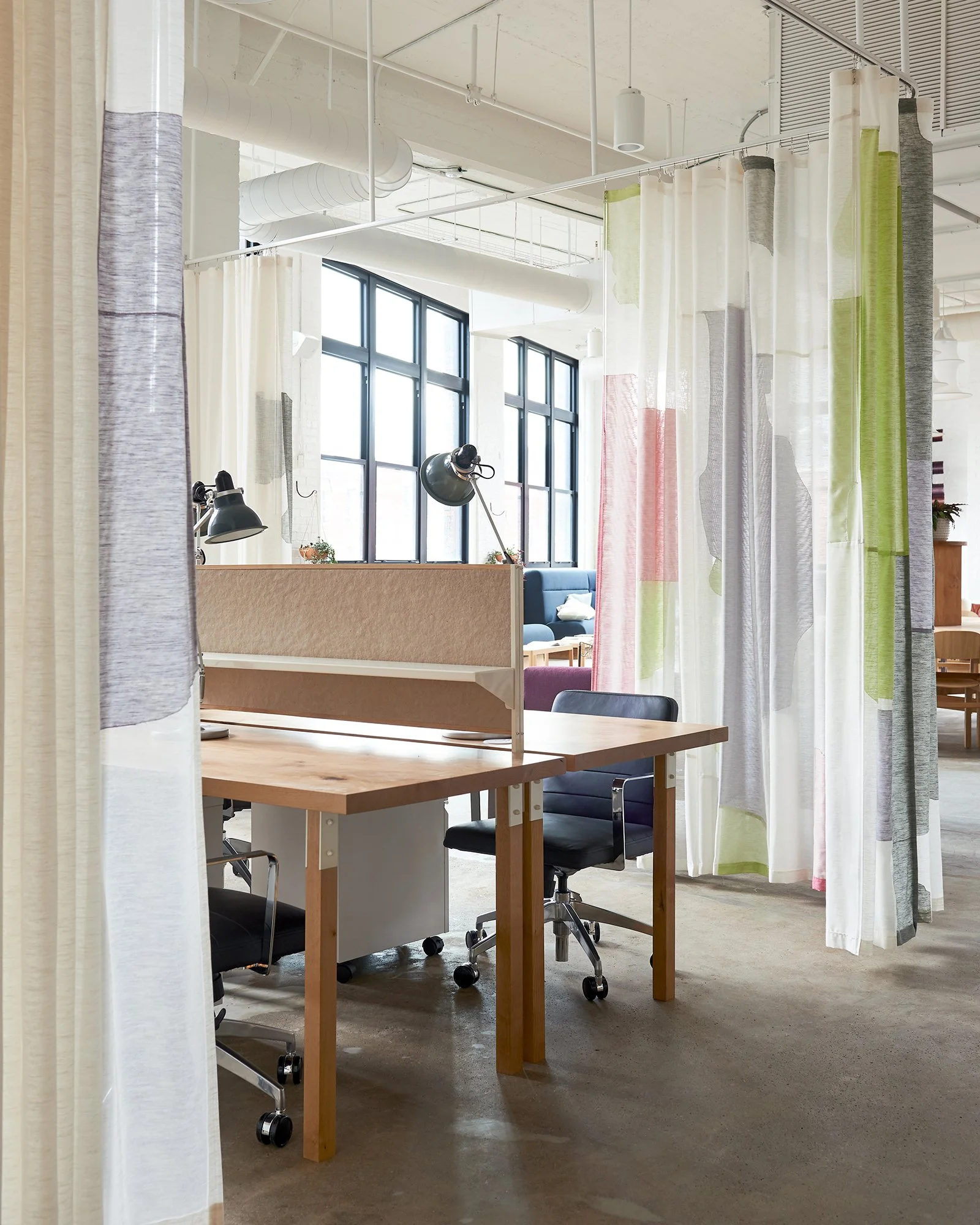Sunlit modern office workspace with desks, black and white desk lamps, an open window, and exposed ductwork on the ceiling.
