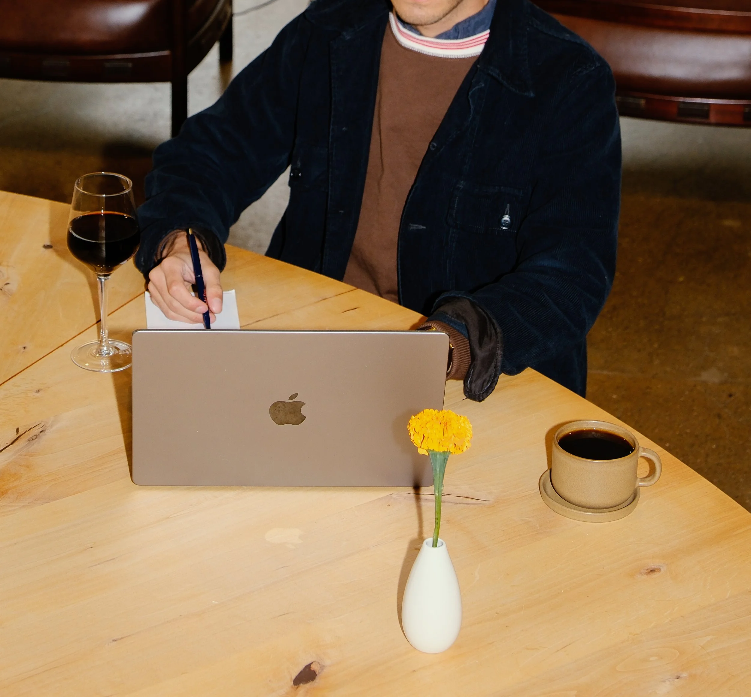 Person sitting in front of laptop working in coworking space with coffee cup and wine