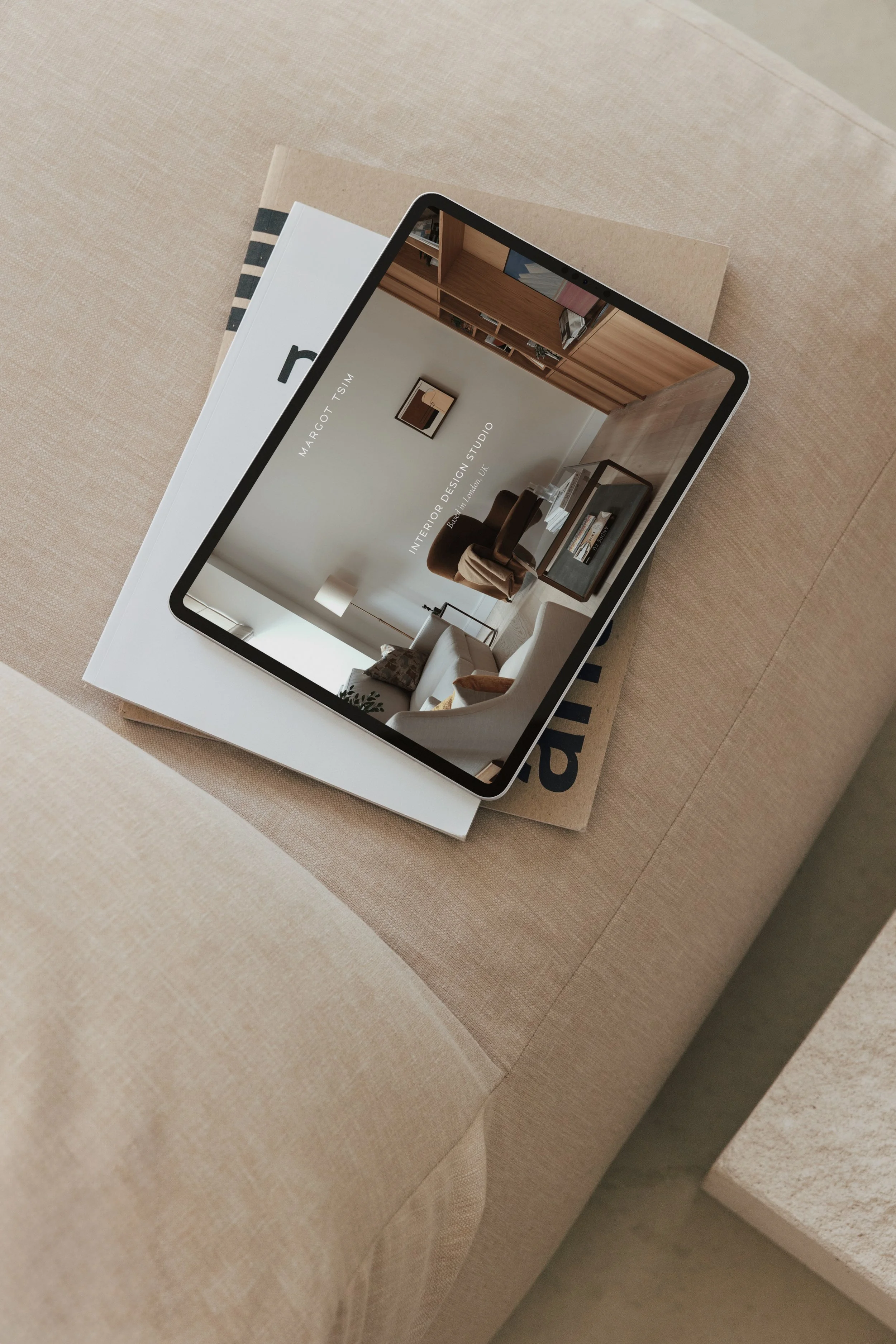 A tablet displaying an interior design photo, placed on top of a closed interior design book on a fabric-covered table.