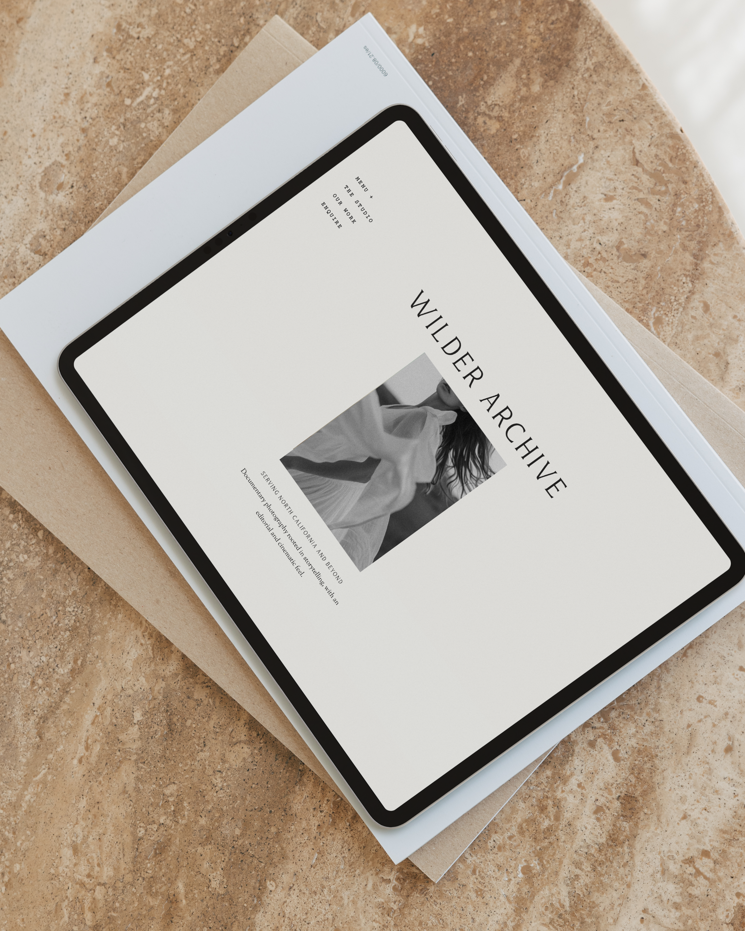 A tablet displaying the website 'Wilder Archive' placed on top of a pile of papers on a stone surface.
