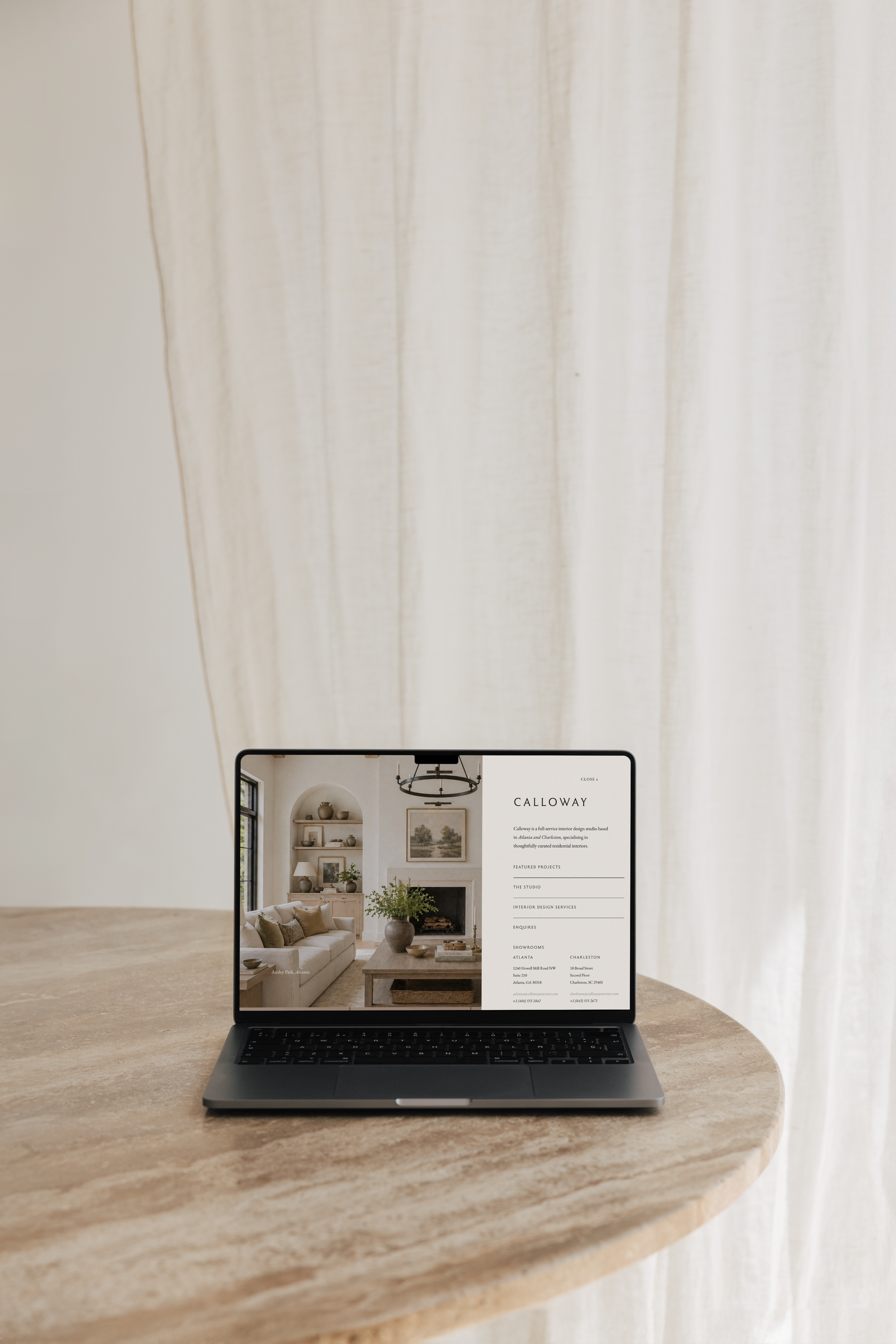 A laptop on a wooden table displaying a webpage for Calloway interior design, showing decorated living room images and contact information.