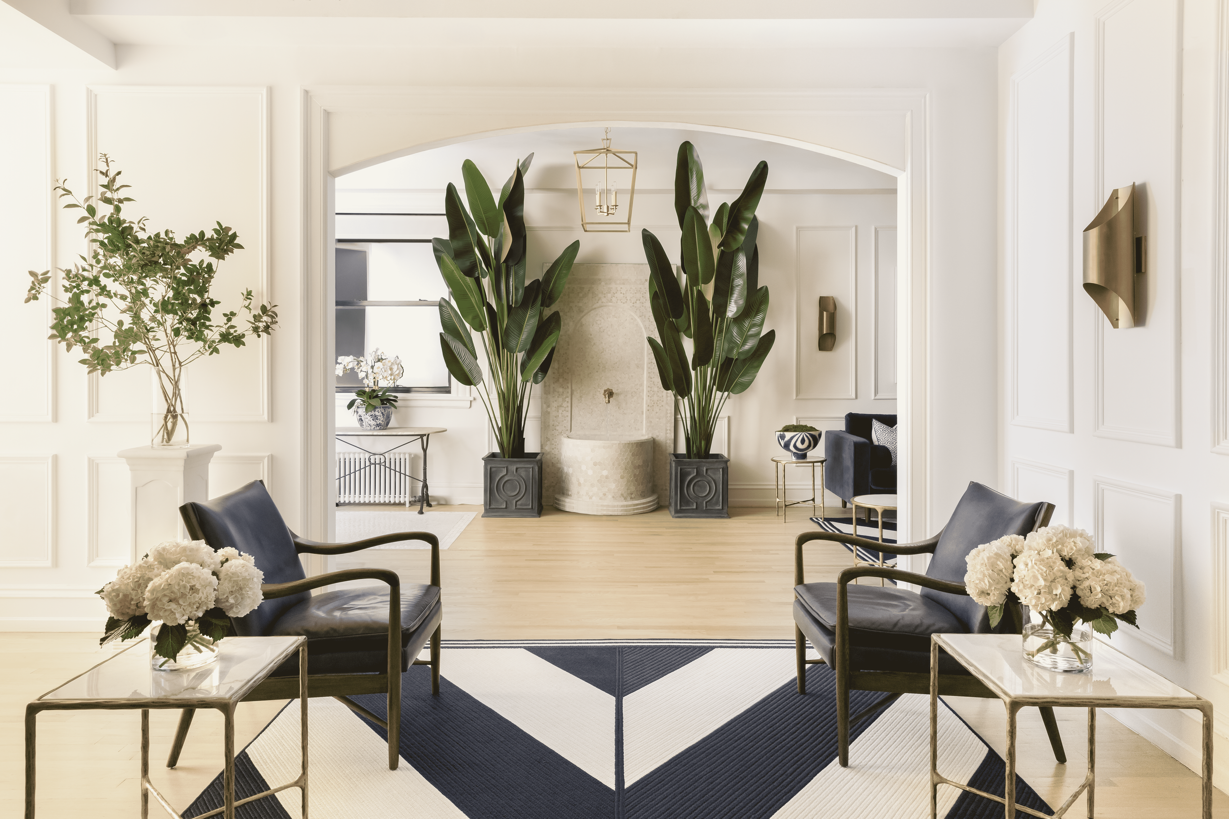 Living room with black armchairs, white floral arrangements, indoor plants, and a fireplace.