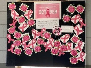 Pink ribbons and pink glittery squares arranged on a black background with an October awareness sign in the center.