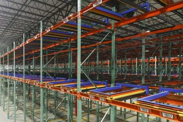 Empty industrial warehouse with orange and green metal warehouse pushback racks.