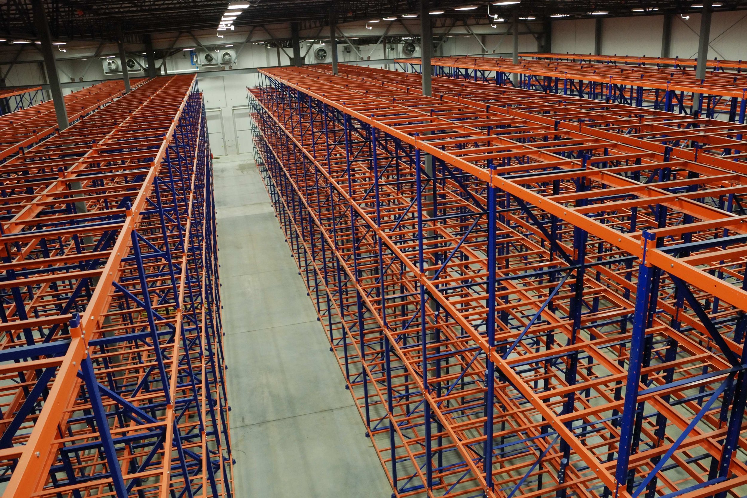 View of empty industrial storage racks with orange and blue pushback racking inside a warehouse.