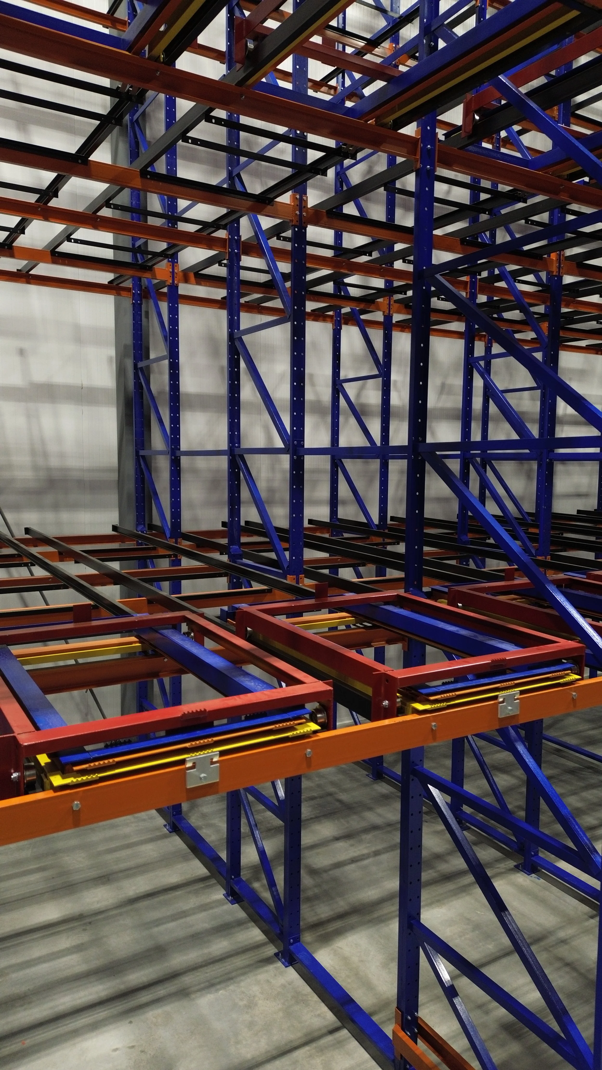 Metal shelving rack structure with multiple levels, painted in orange, blue, and black, inside a warehouse or large storage area.