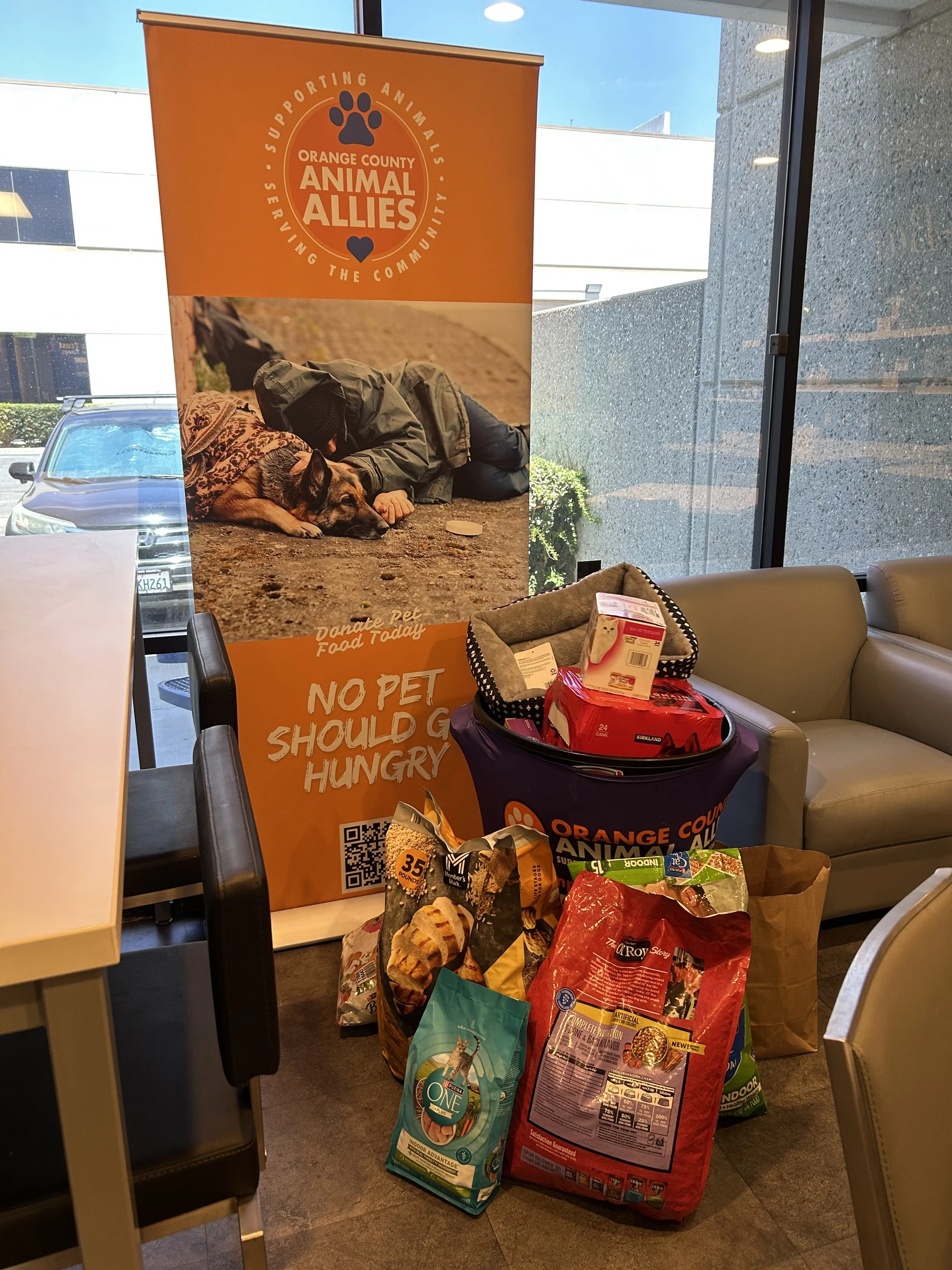 A bin full of dog and cat food beside a banner reading Orange County Animal Allies.