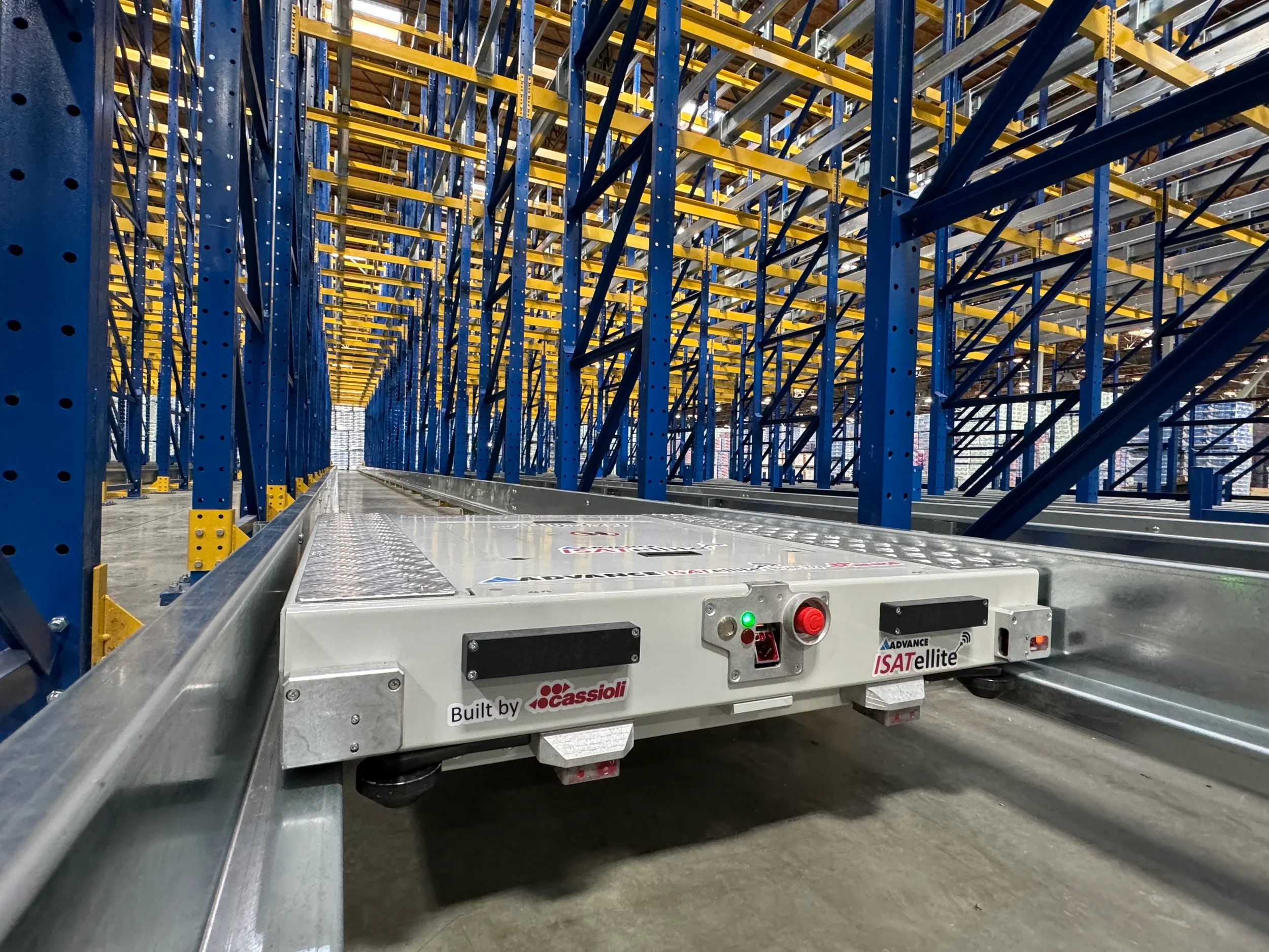 Industrial warehouse shelving system with blue and yellow metal racks. A robotic automated guided vehicle (AGV) with