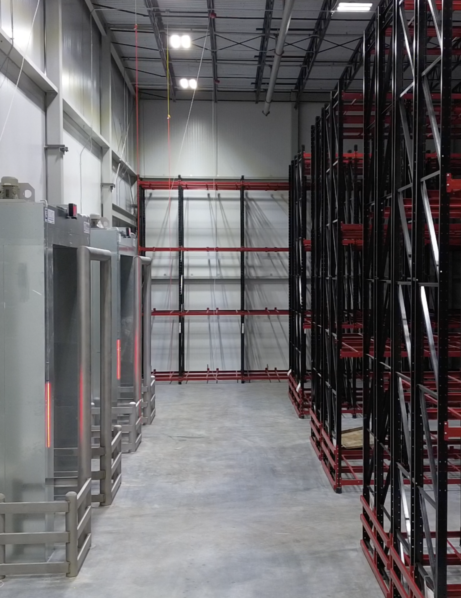 Interior of a warehouse with empty shelving units on the right and a pallet rack on the left, with a polished concrete floor and fluorescent ceiling lights.