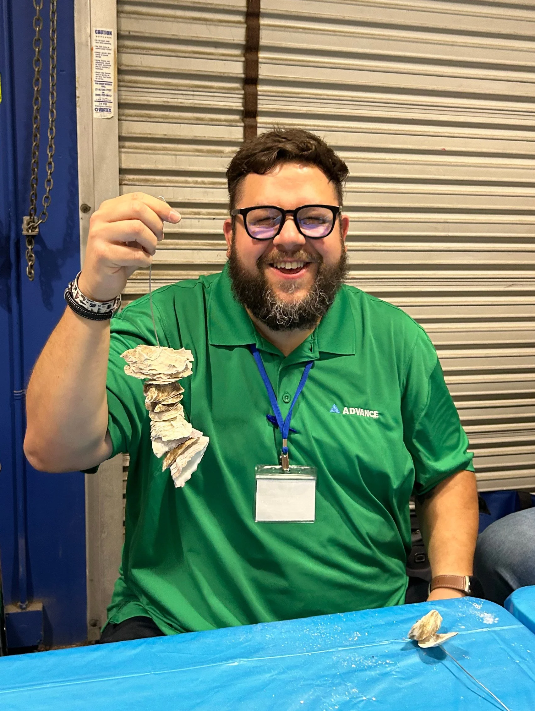 Smiling man holds up string of oyster shells on a metal wire.