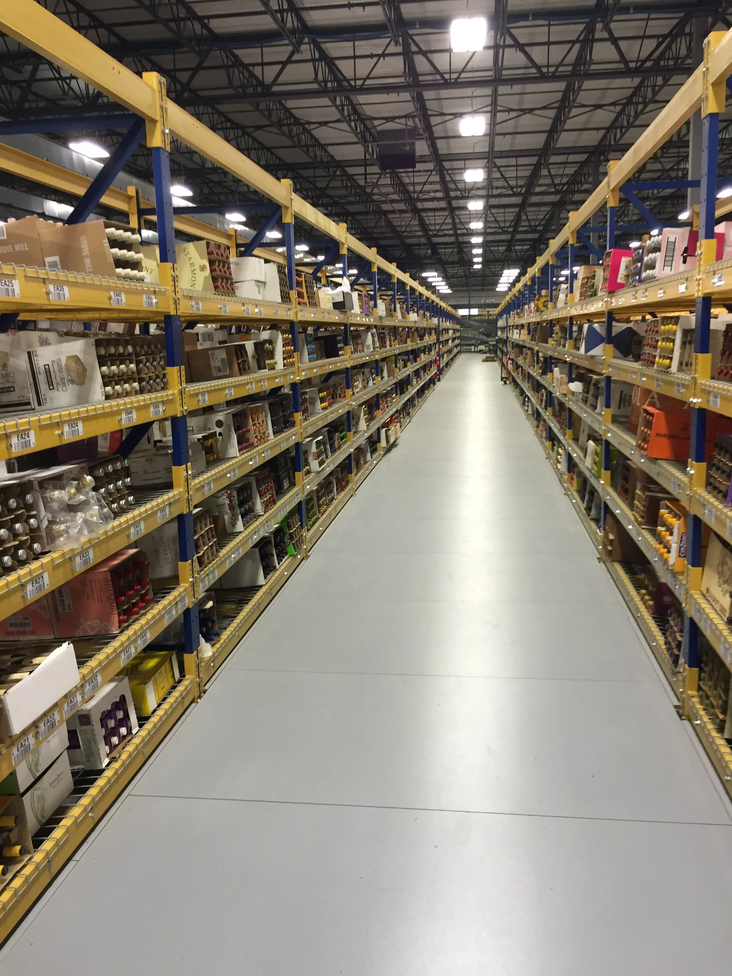 Guided shot of an aisle in a warehouse-style store with metal shelves stocked with various products on both sides.