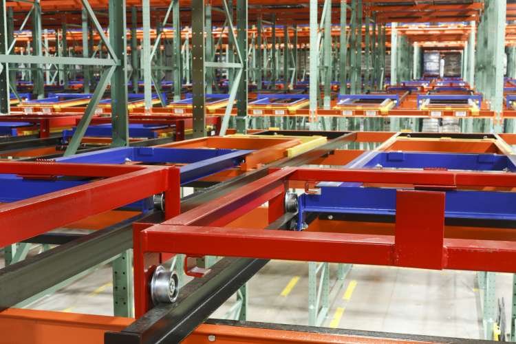 Industrial warehouse pushback shelving units with empty blue and orange bins on multiple levels.