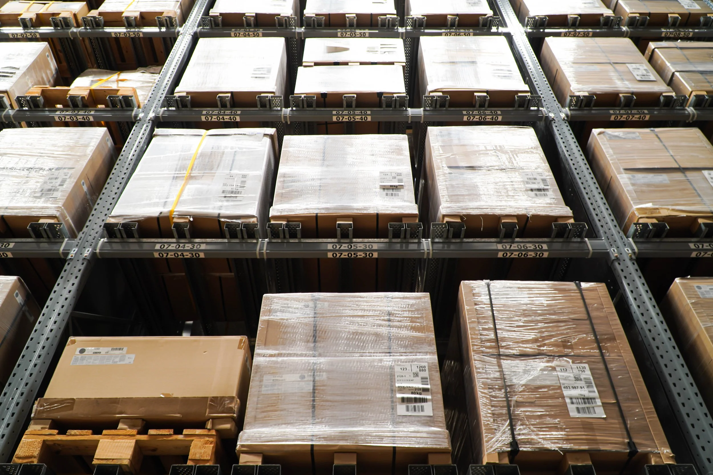 Palletized cartons stored in a high-density warehouse storage system with organized storage lanes and location labels.