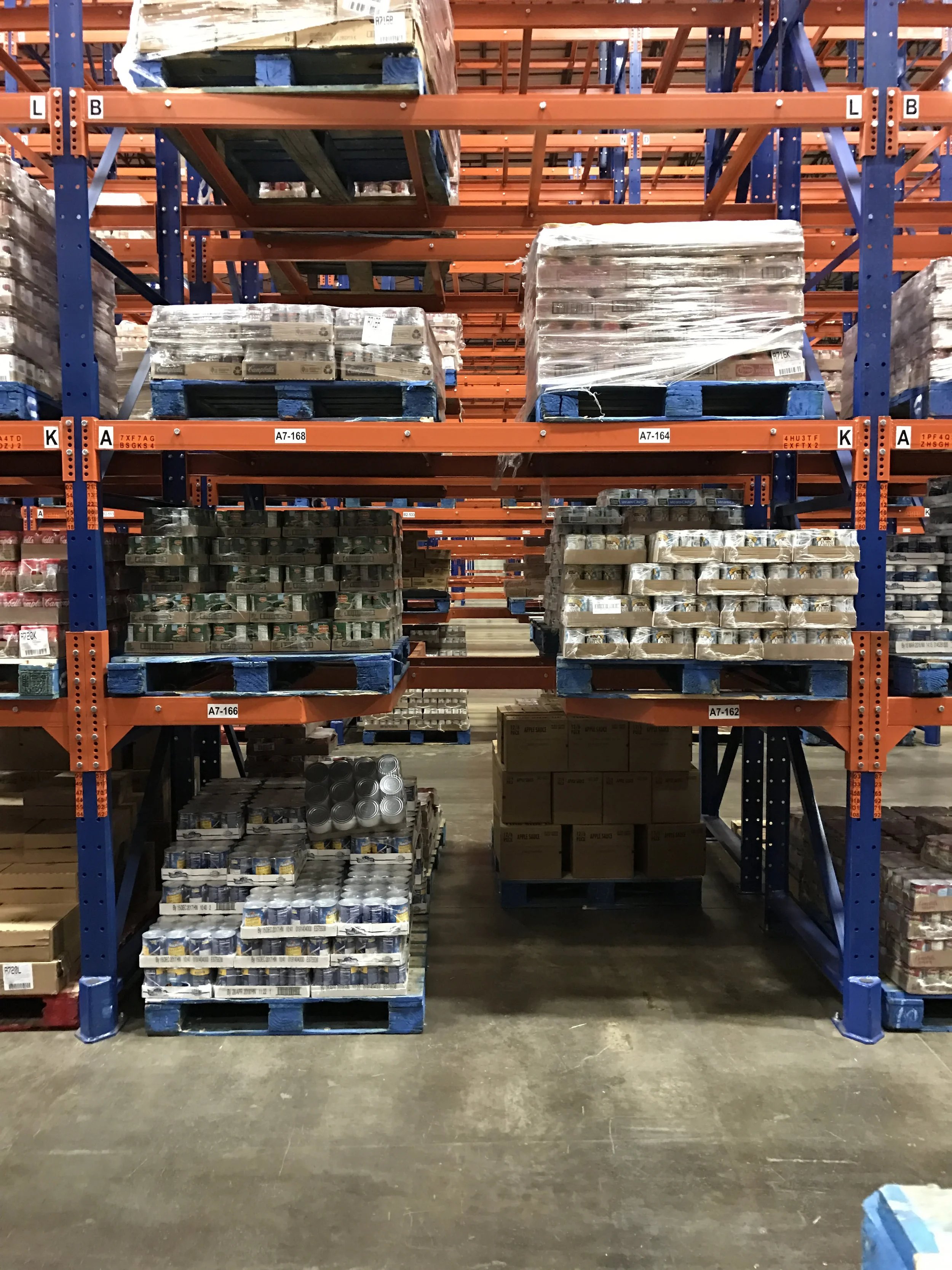 Warehouse aisle with metal shelving filled with boxes and cans stored on pallets.