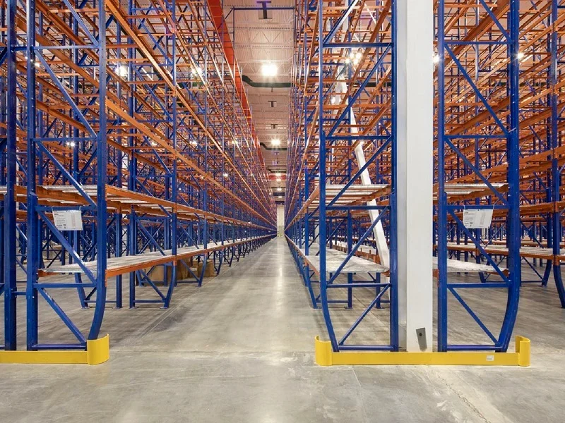 Empty warehouse with tall blue and orange industrial shelving units and a wide central aisle.