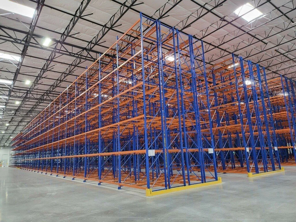 A warehouse aisle with shelves stocked with crates of apples and other fruits and vegetables.